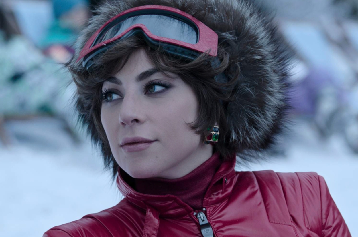 A person in a fur-trimmed ski jacket and goggles looks off-camera in a snowy setting