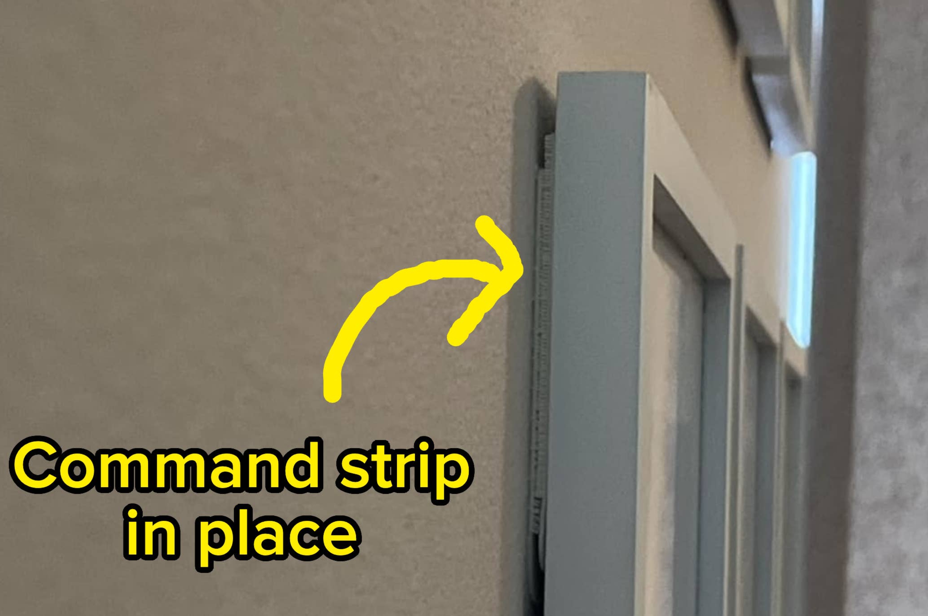 Command strip holding a picture frame on a wall, shown with an arrow pointing to it. Text reads: "Command strip in place."