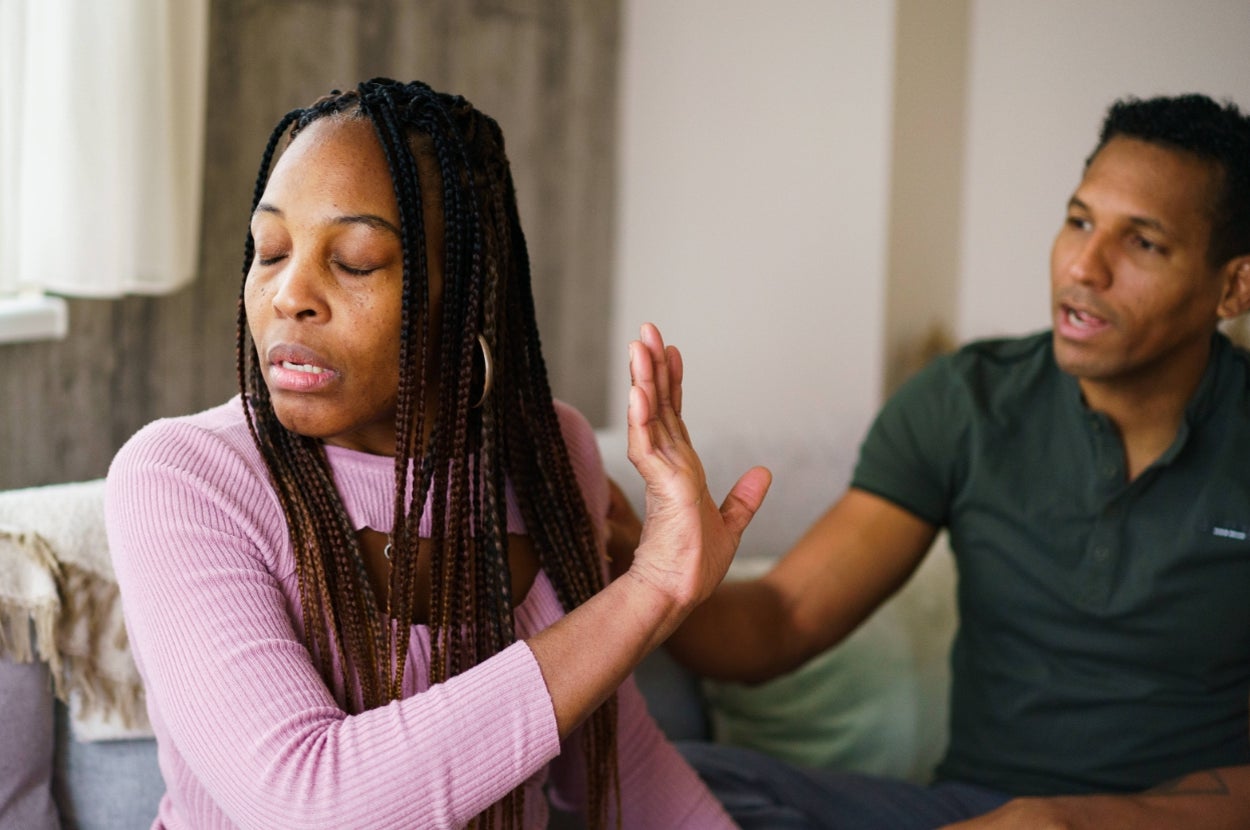 Two people sitting on a couch; one is raising a hand, appearing to refuse or dismiss what the other is saying
