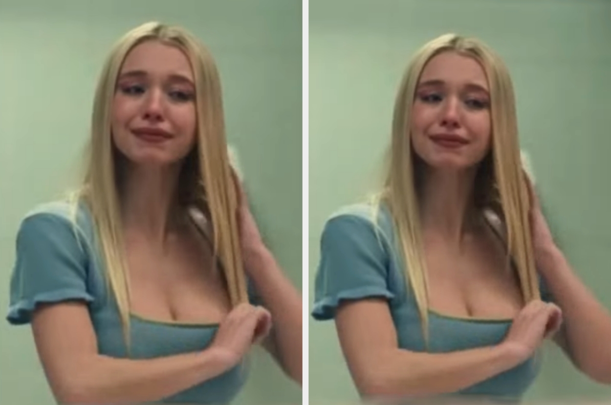 Woman with long hair in a blue top looking emotional in front of a mirror. She appears to be upset or crying