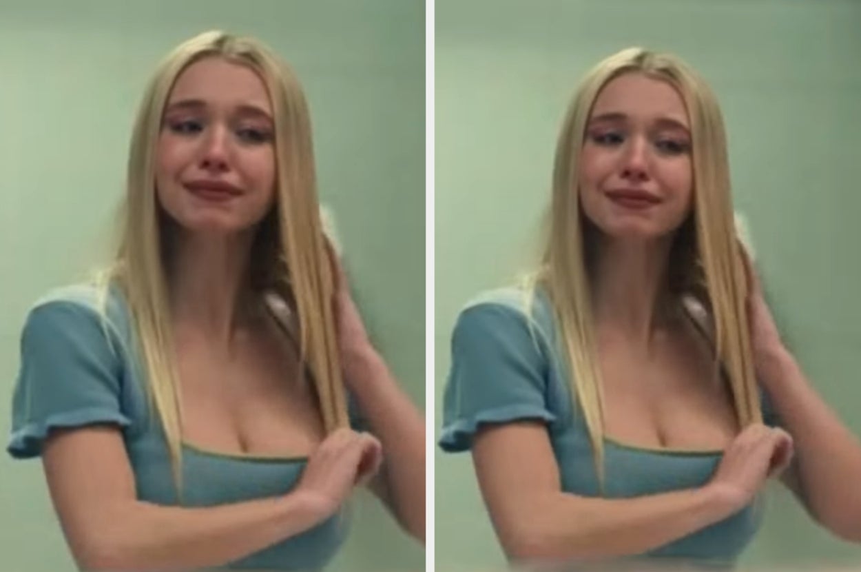 Woman with long hair in a blue top looking emotional in front of a mirror. She appears to be upset or crying