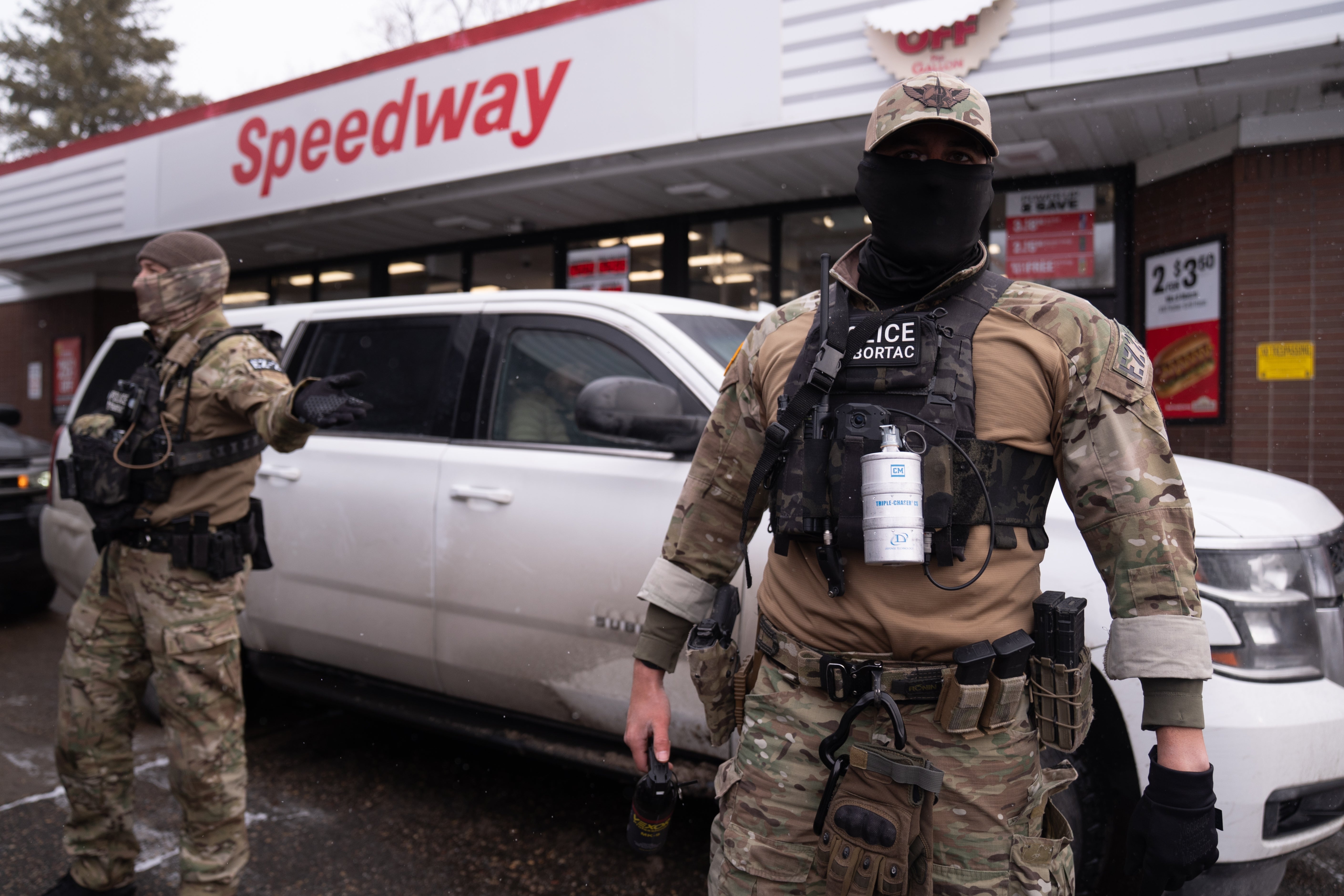 Bevæpnede offiserer i taktisk utstyr står foran en nærbutikk med 