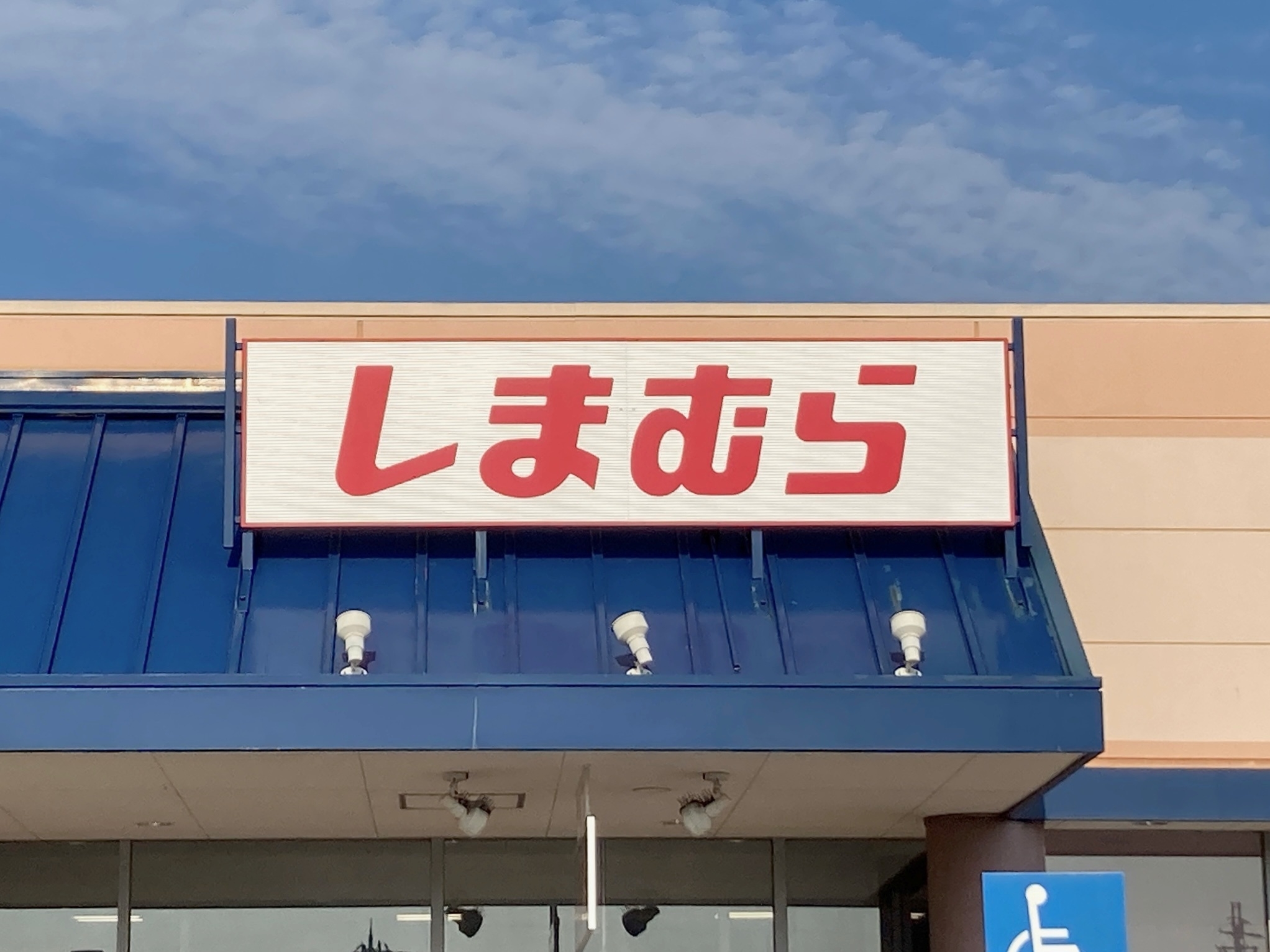 The image shows a store sign with Japanese characters atop a building under a partly cloudy sky