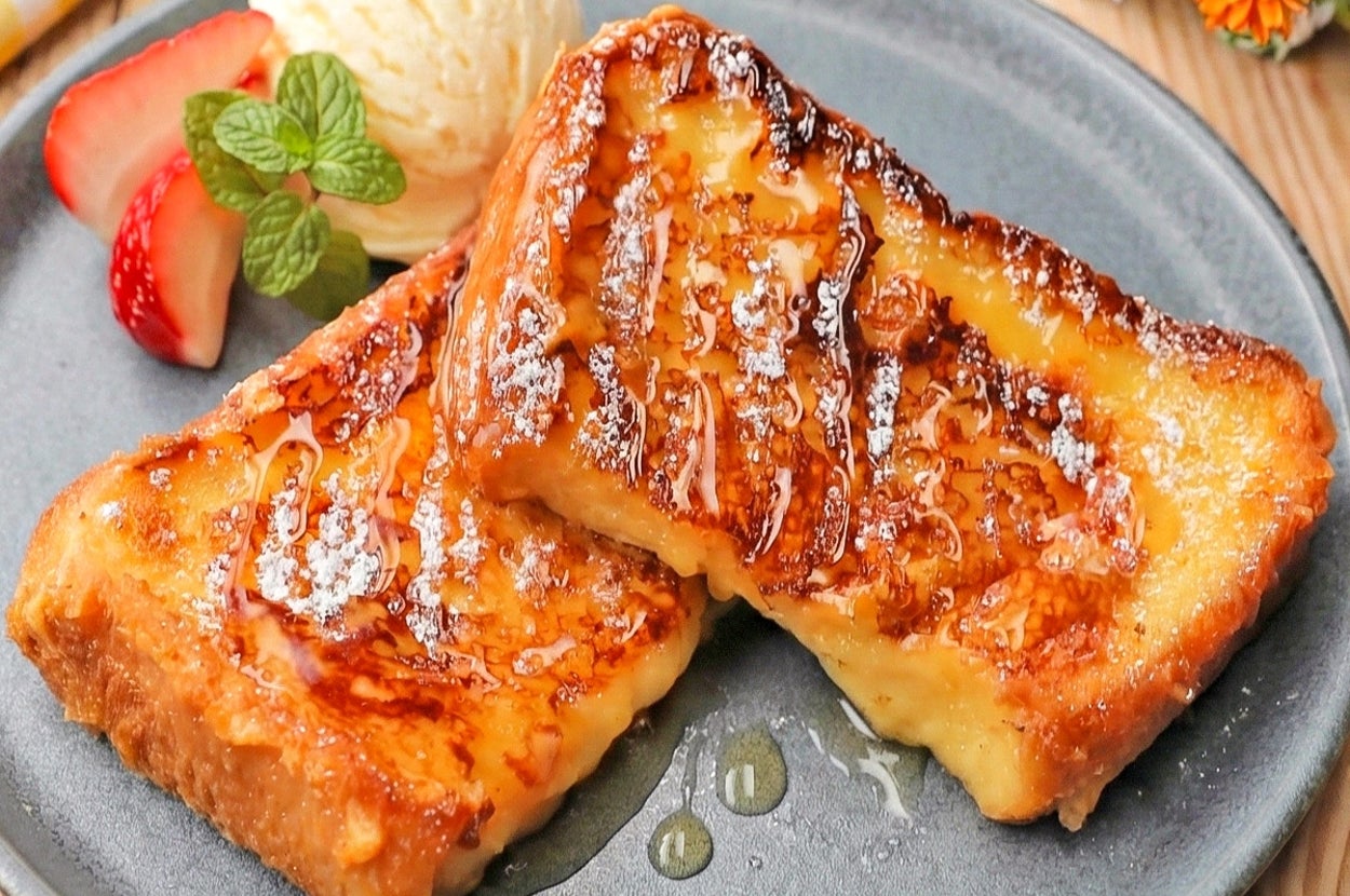 フレンチトースト2枚が黒い皿に盛り付けられ、バニラアイス、イチゴ、ミントが添えられている。