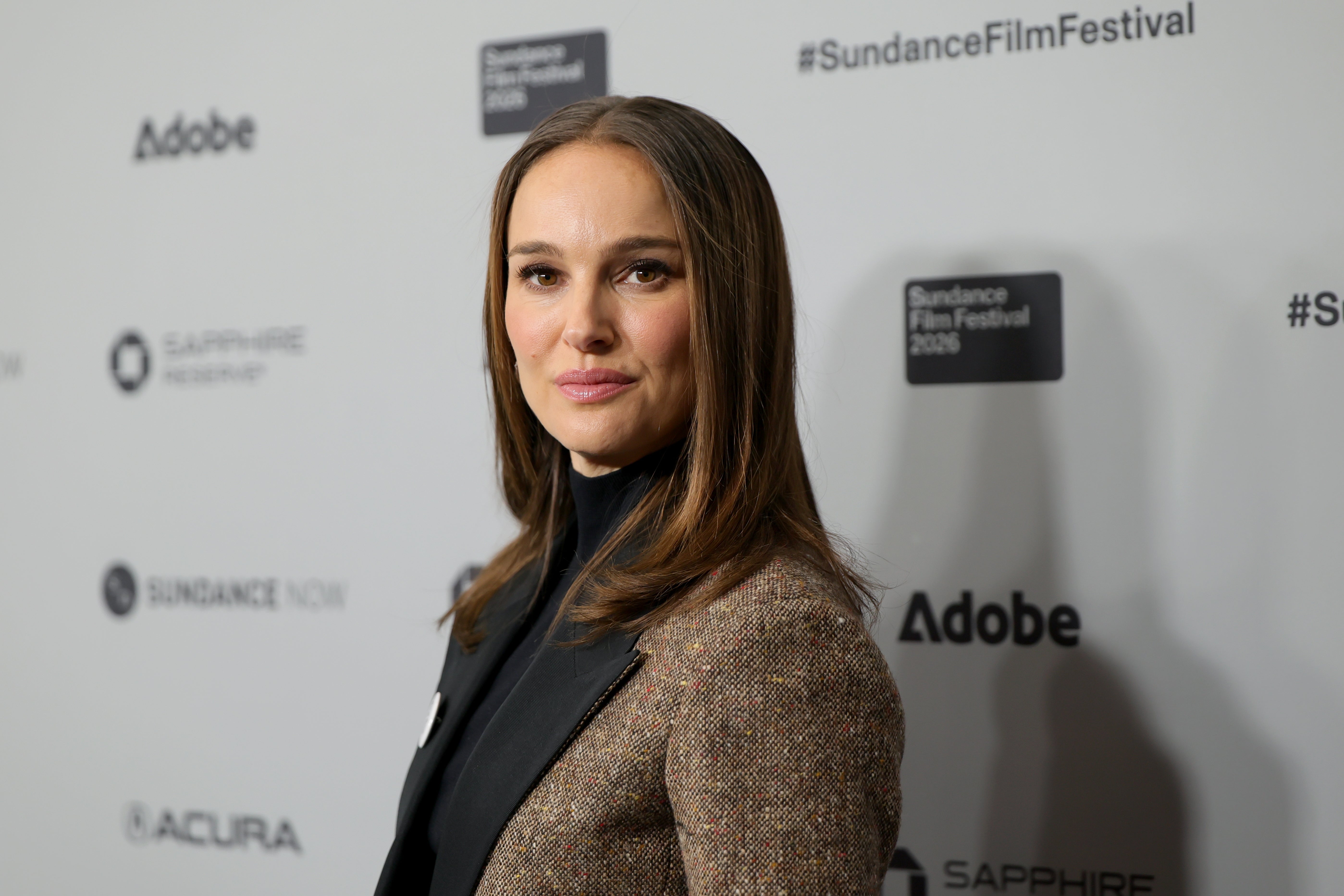 Person i en skreddersydd dressjakke over en svart topp poserer på en Sundance Film Festival-begivenhet i bakgrunnen