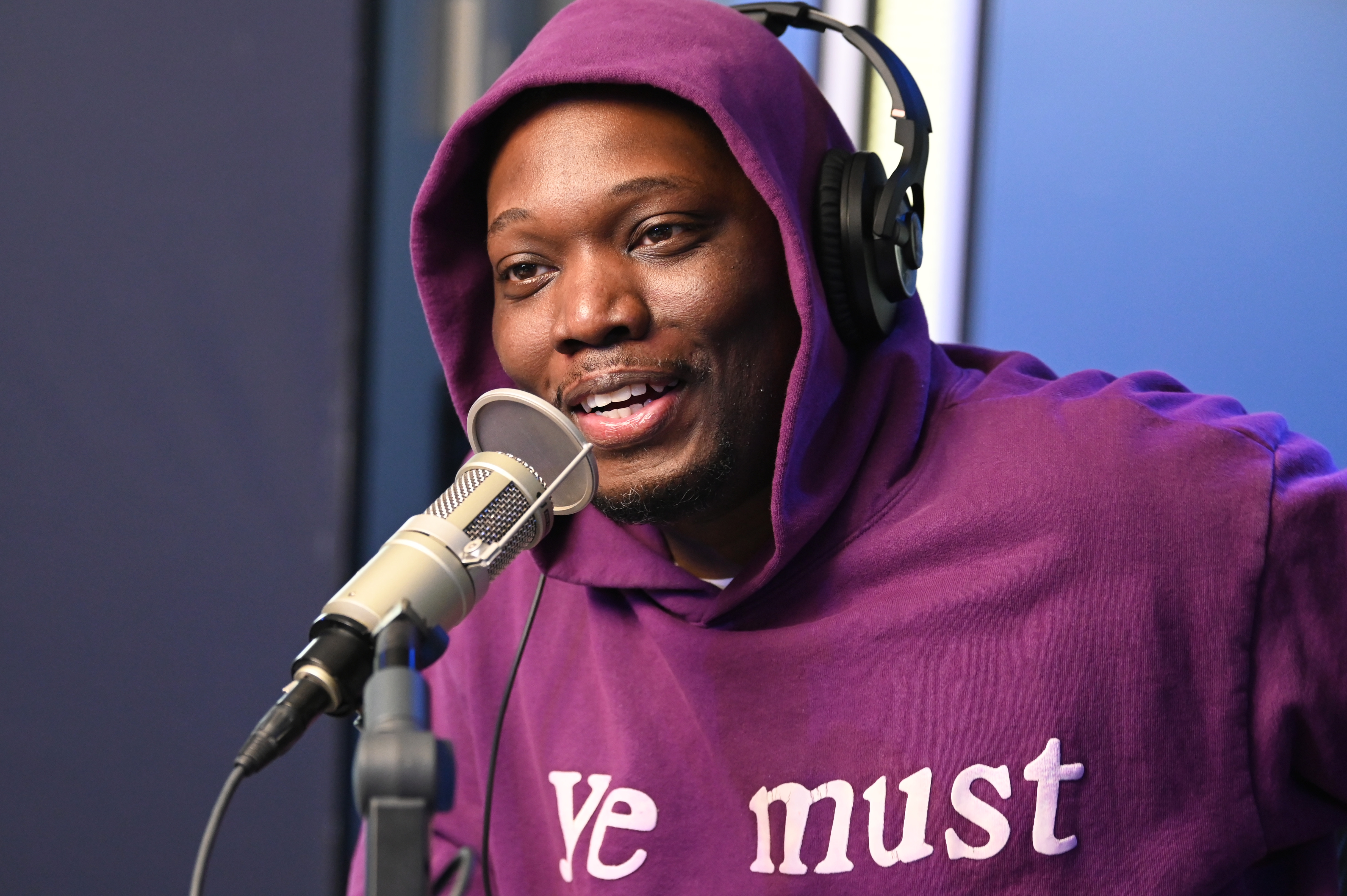 Michael Che i en hettegenser med hodetelefoner snakker i en mikrofon under en opptaksøkt