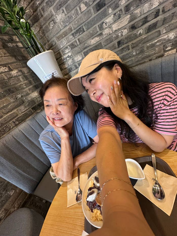 A mother and her daughter smiling at a cafe table, taking a selfie with desserts in front of them