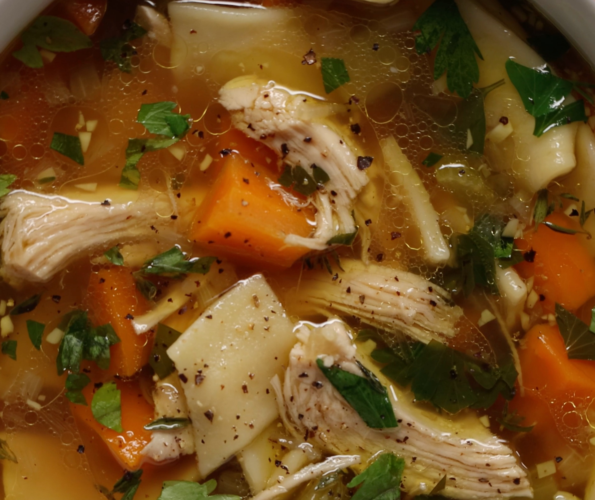 Bowl of hearty chicken noodle soup with chunks of carrot, noodles, and herbs on top