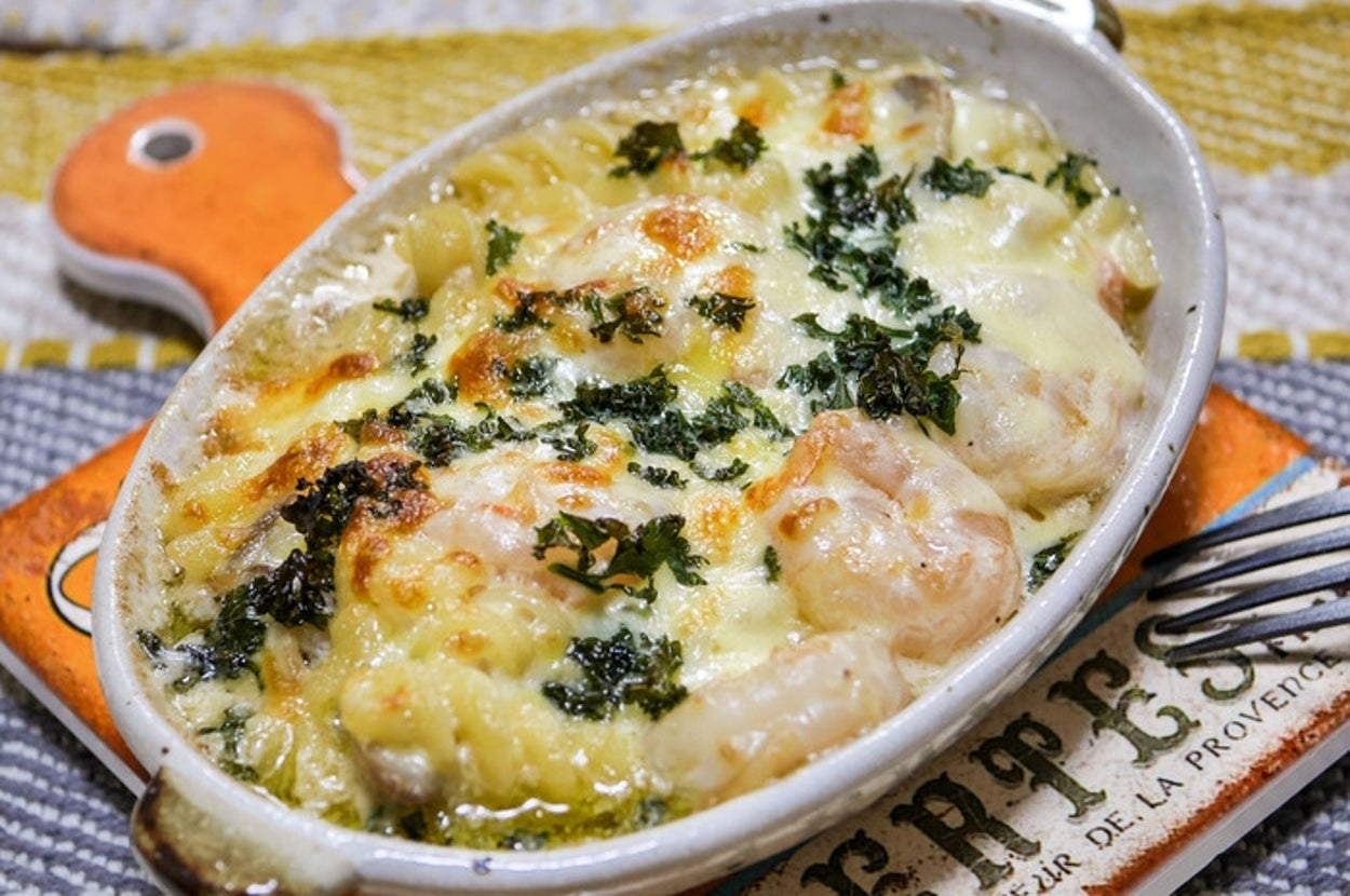 グラタン皿に盛られたエビとチーズのグラタンがあり、焼き色がついておいしそうに見える。