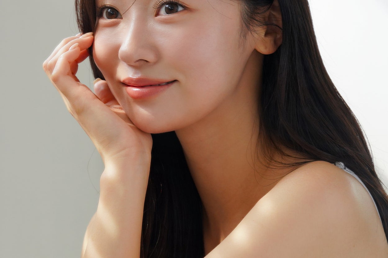 女性が微笑んで窓辺に座っている、カジュアルなタンクトップ姿。リラックスした雰囲気。