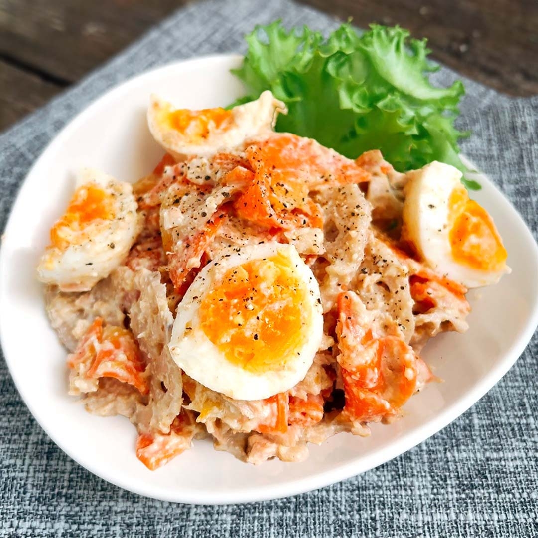 ゆで卵とにんじんがトッピングされたクリーミーなサラダが白い皿に盛られ、リーフレタスが添えられています。