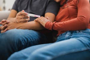A couple sits closely on a couch, with one holding a positive pregnancy test, signifying a shared, intimate moment