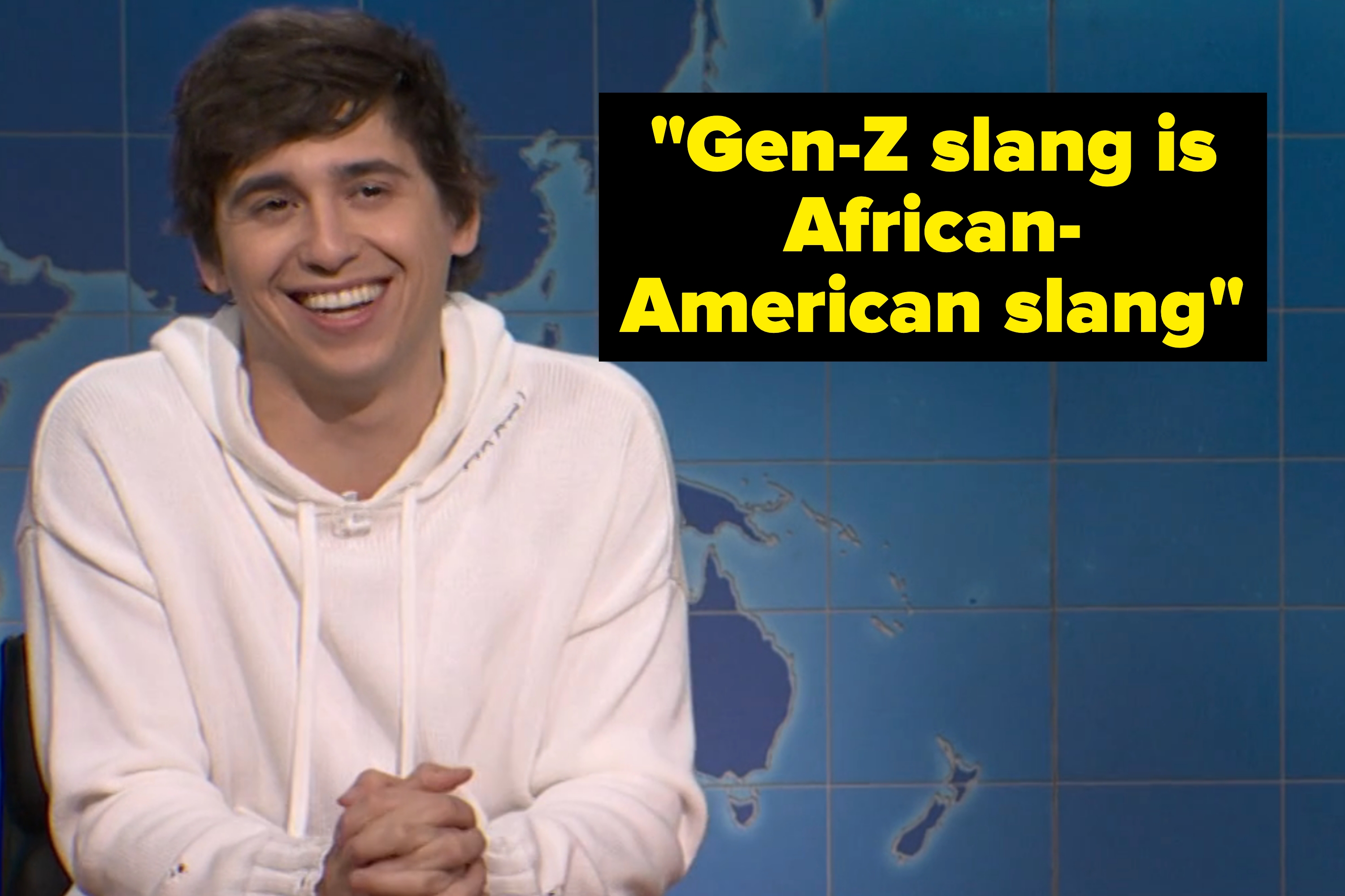 Two people, one in a casual hoodie and the other in a suit and tie, share a laugh behind a news-style desk with a world map backdrop