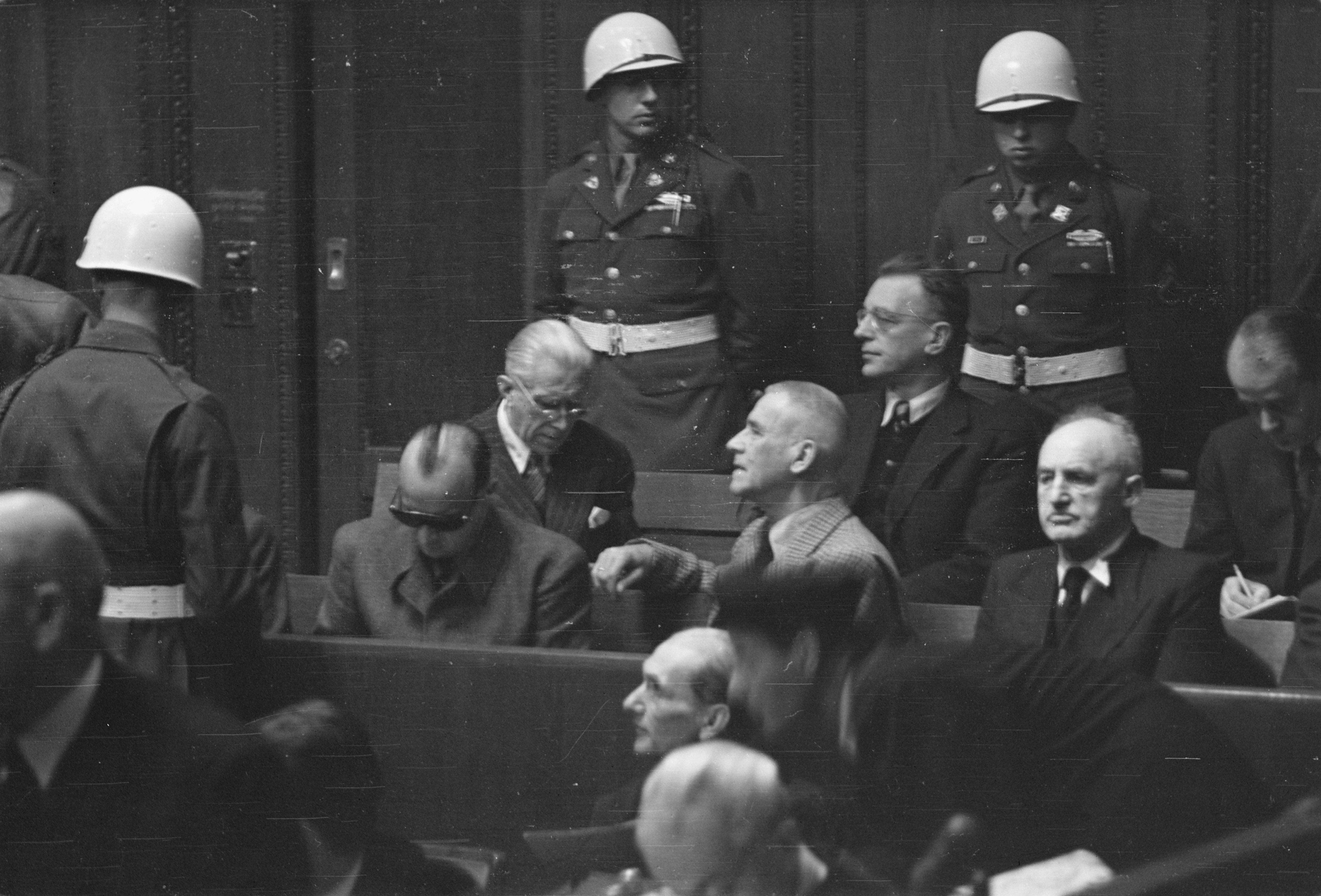 Historisk rettssalsscene med menn i dress og militært personell