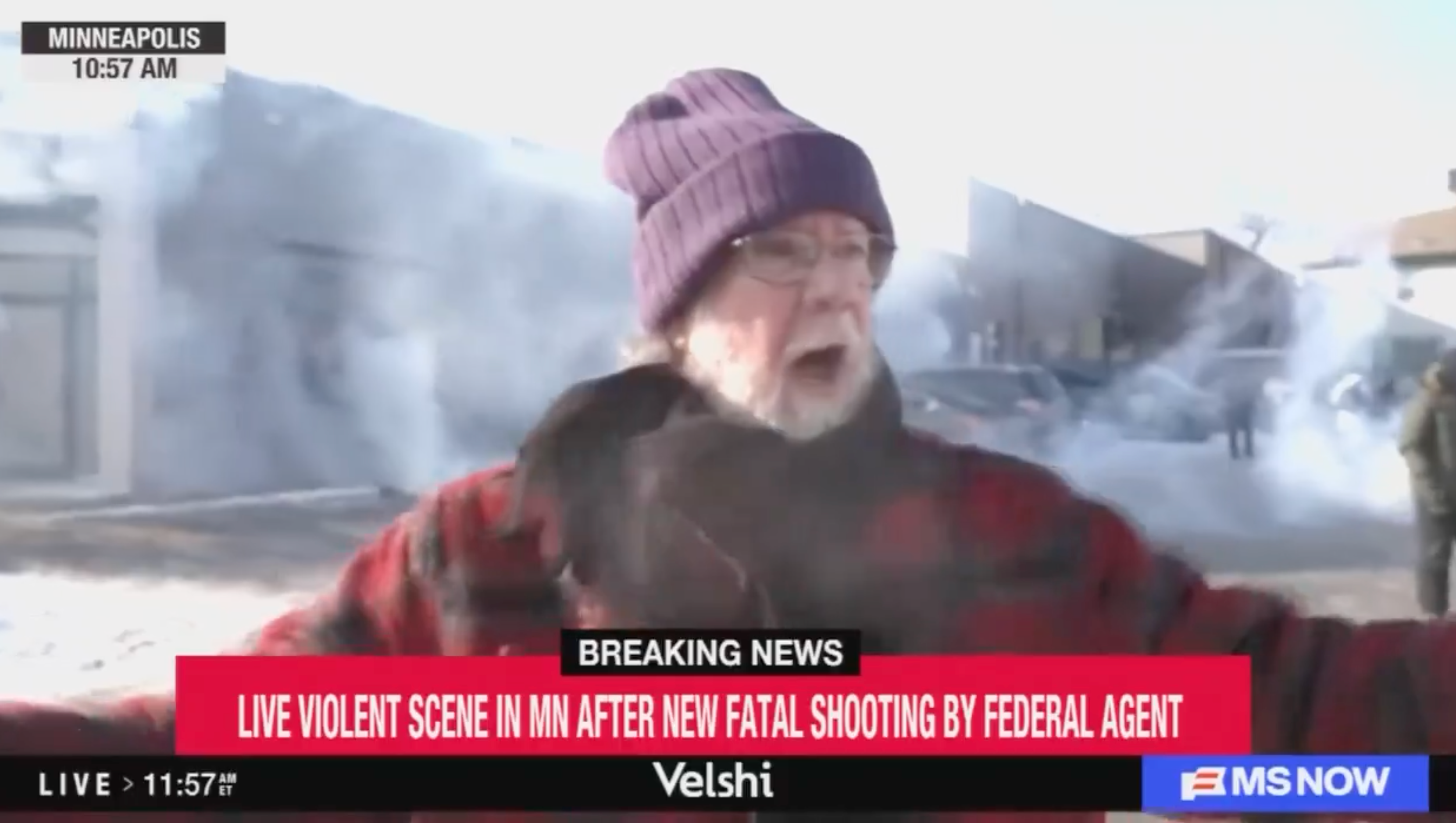 En mann i frakk og hatt snakker ettertrykkelig på en snødekt gate. Breaking news ticker nevner et skyting av en føderal agent i Minnesota