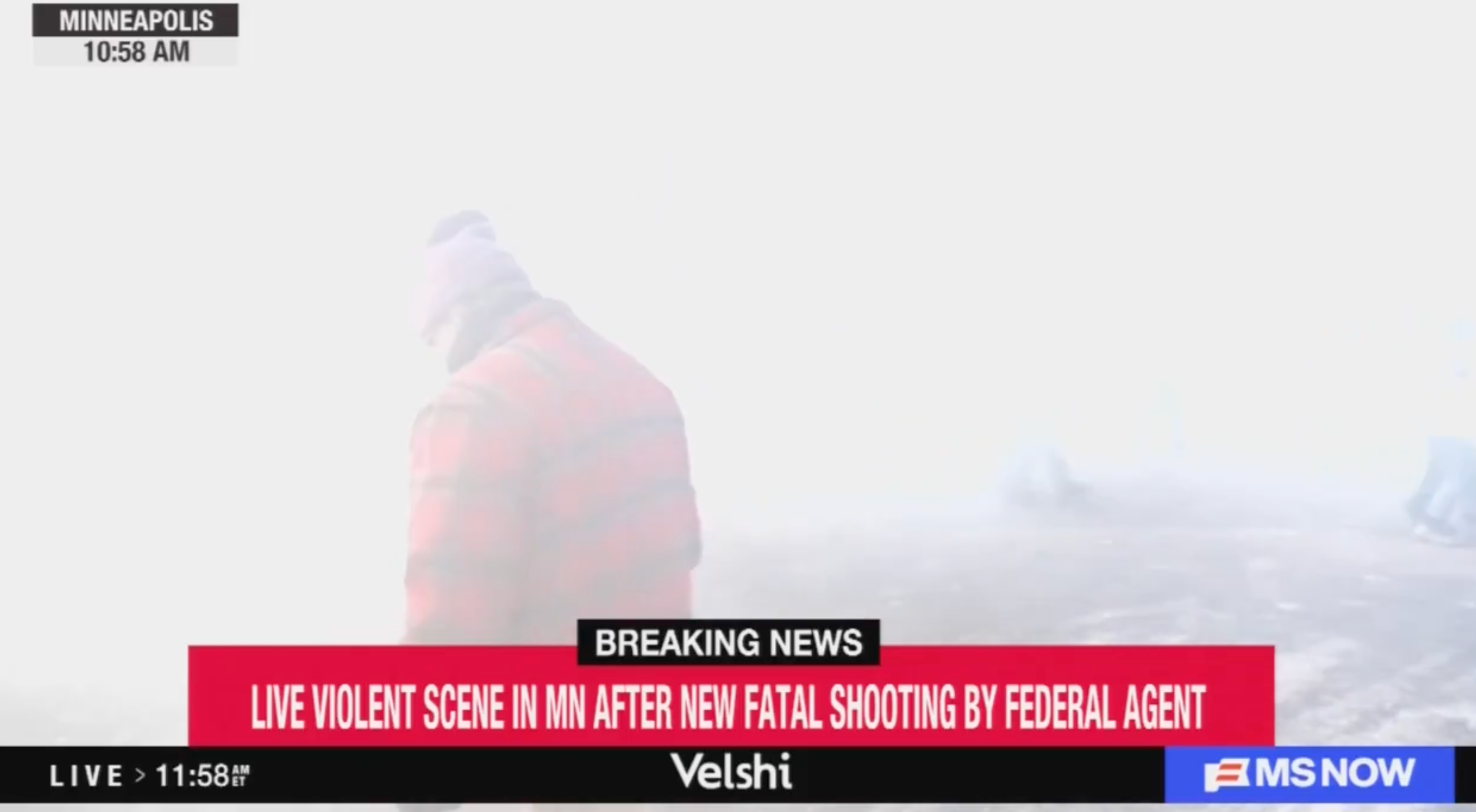En person i vinterfrakk står i tåkete forhold. Skjermen viser siste nyheter om et skyting med en føderal agent i Minneapolis