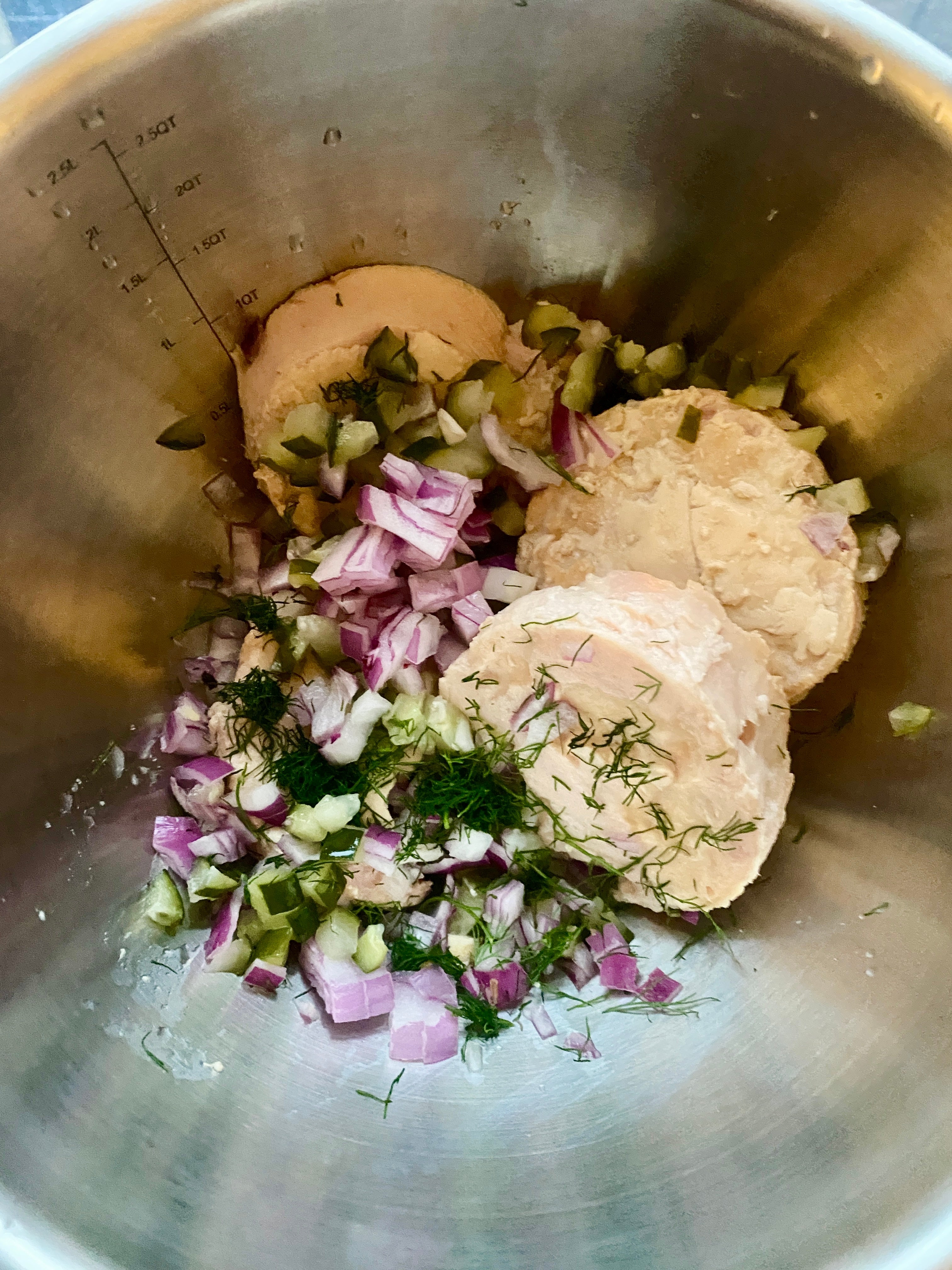 Ingredients in a mixing bowl: chicken, diced red onion, chopped pickles, and dill, ready for preparation