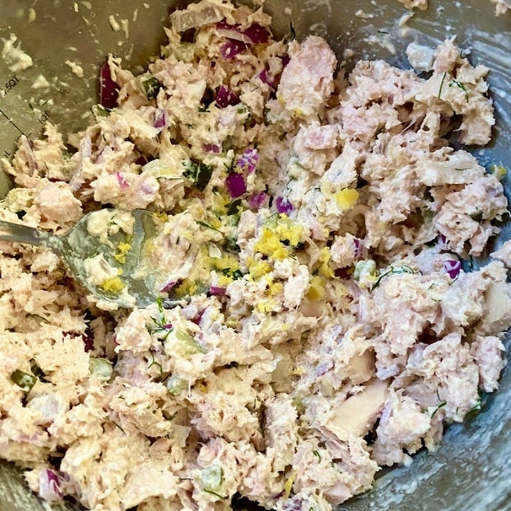 A bowl of tuna salad with chopped onions and other mixed ingredients, with a spoon partially visible