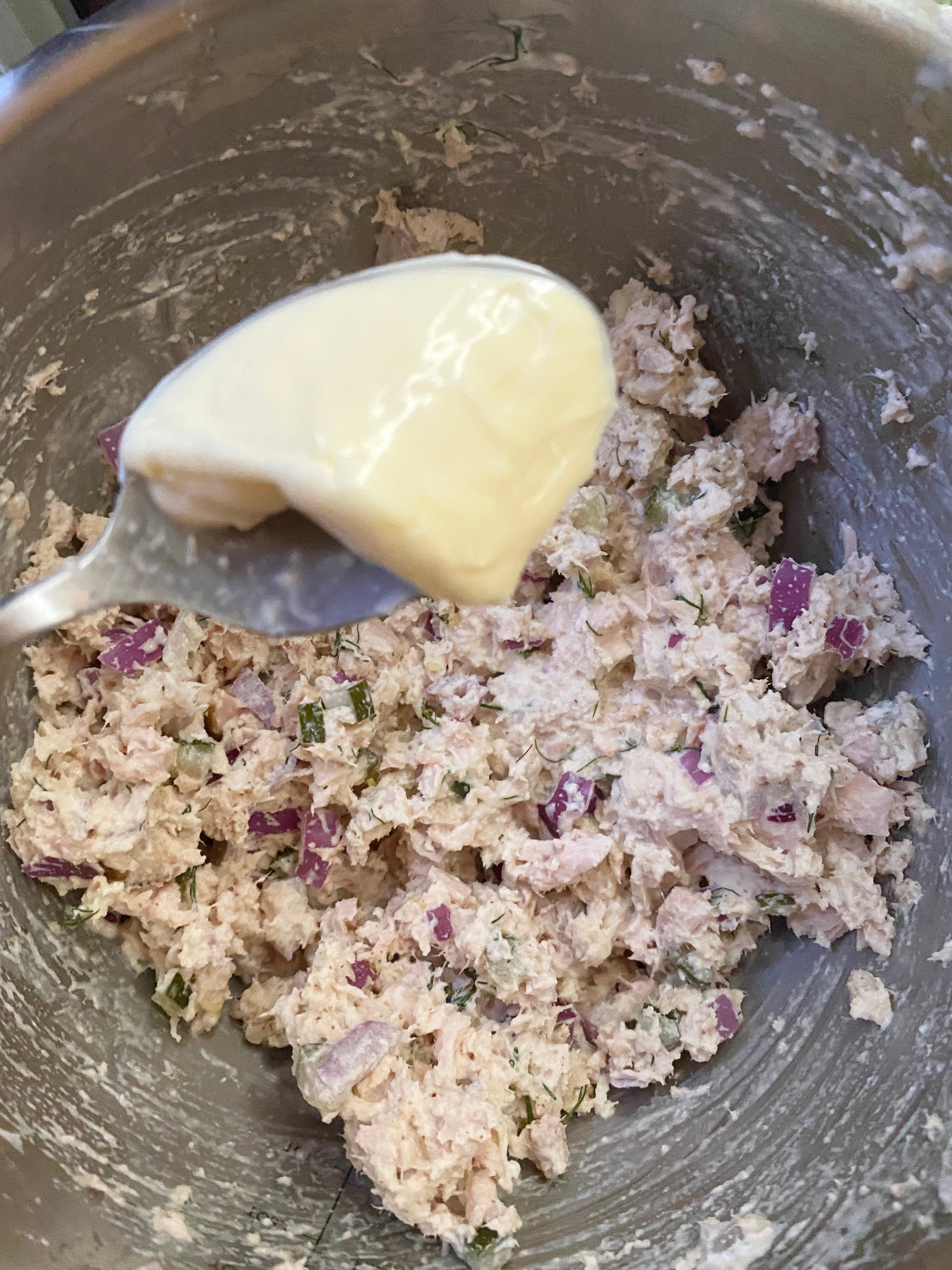Bowl of mixed chicken salad with red onions and herbs; a spoon with mayonnaise is held above