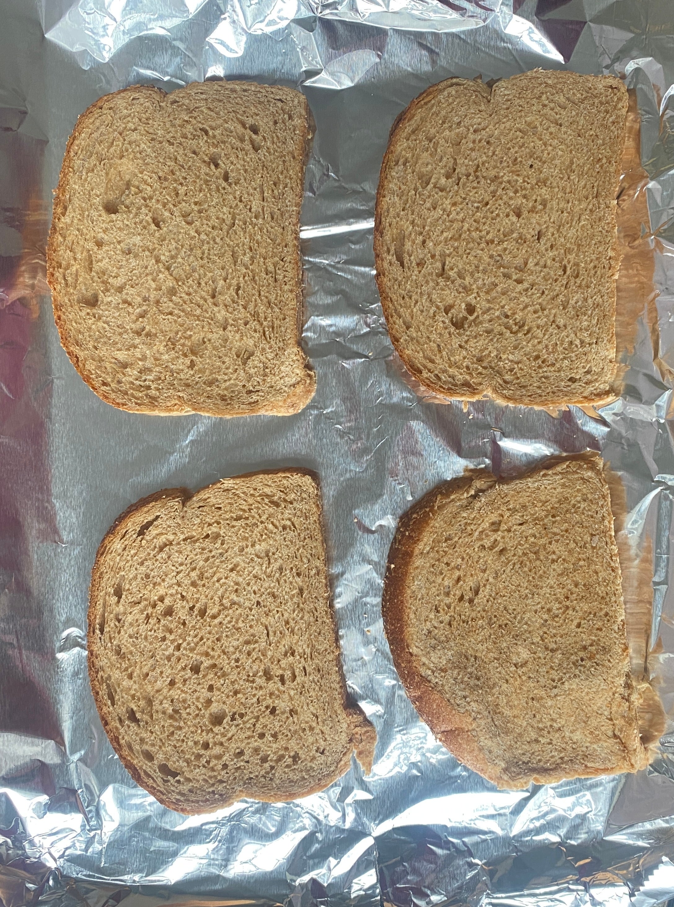 Four slices of bread on a foil-lined baking tray, ready for toasting