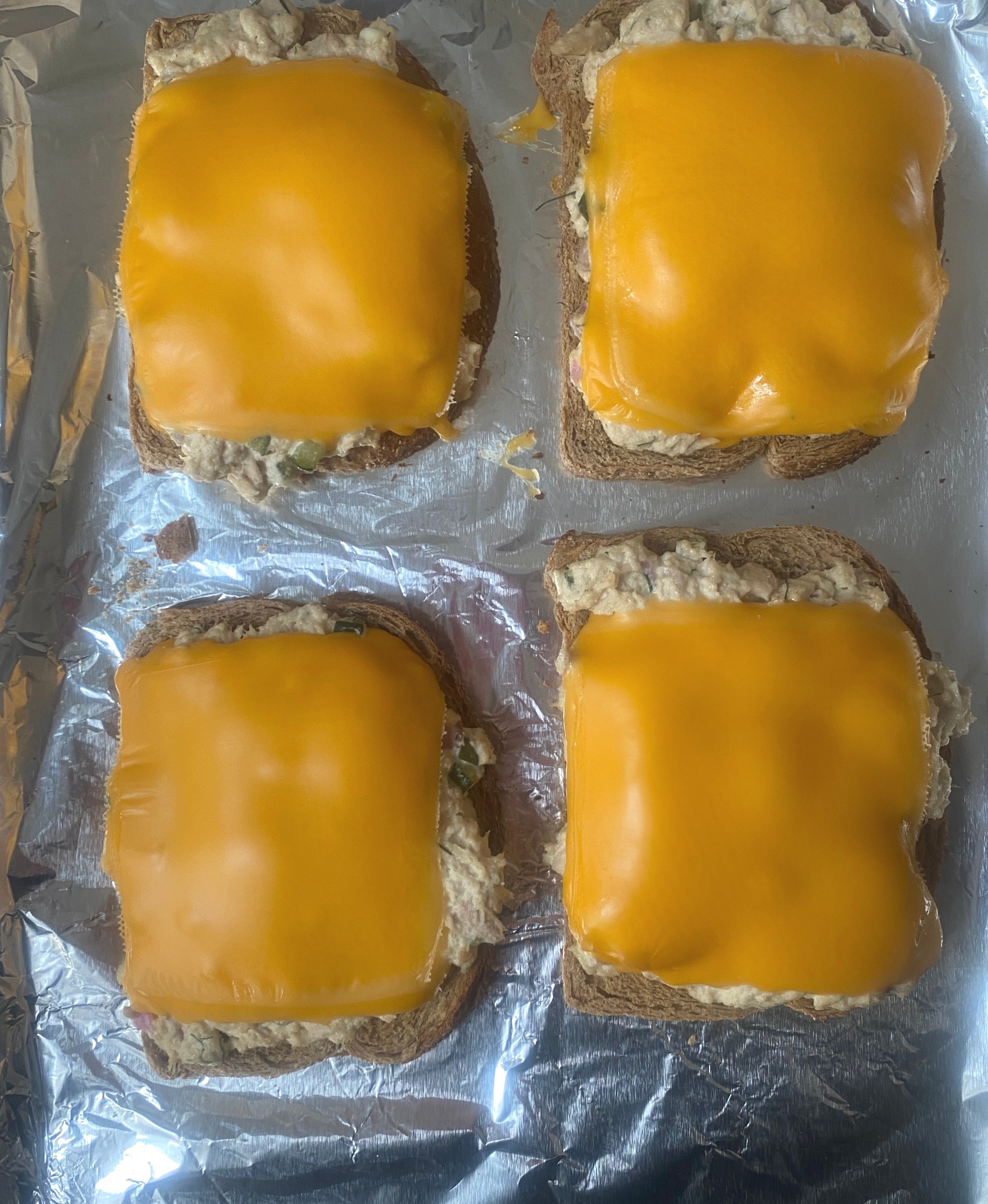 Four open-faced tuna melts topped with melted cheese on foil