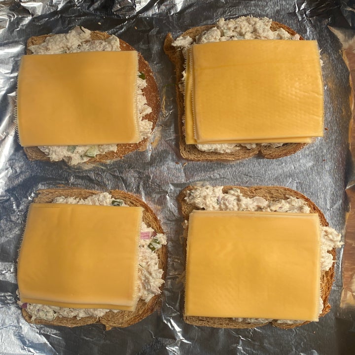 Four open-face tuna melts with cheese slices on bread on a foil-lined tray