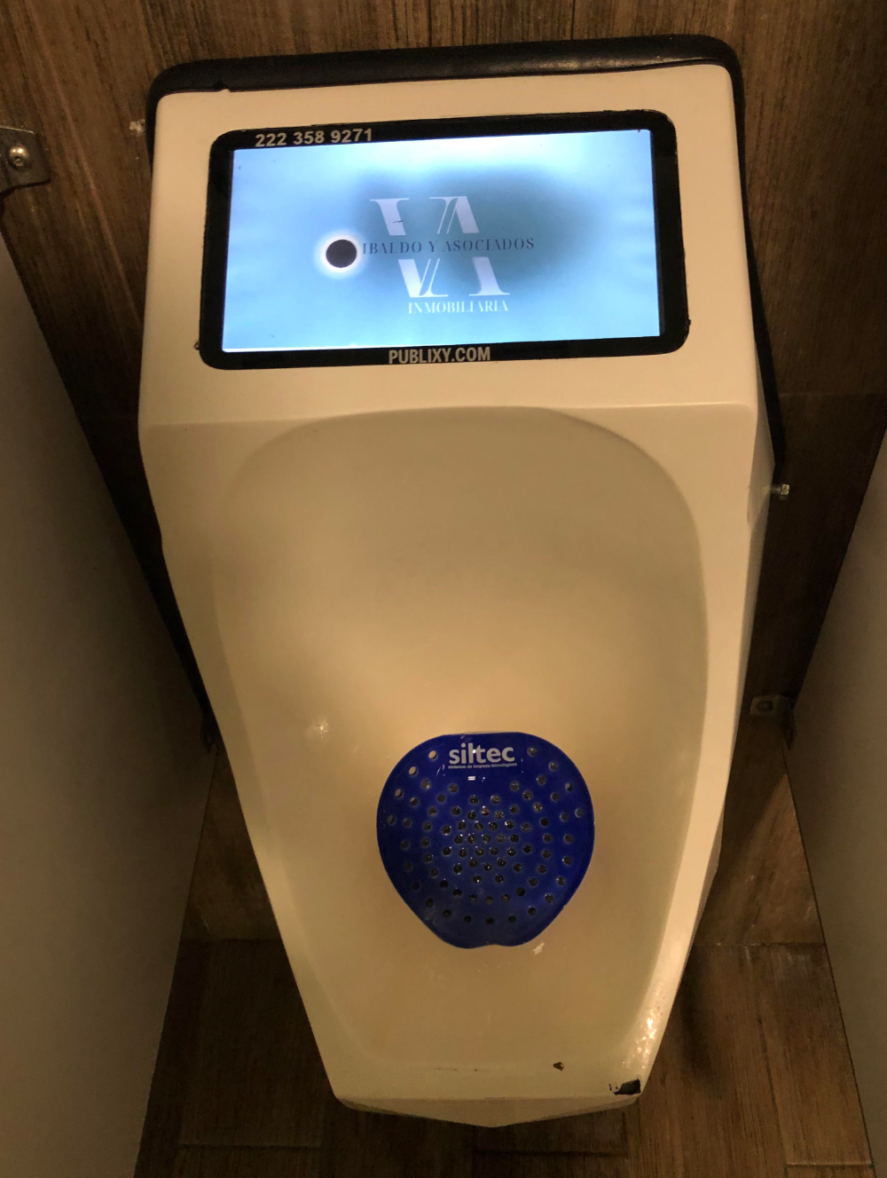 Digital screen above a urinal displaying an advertisement
