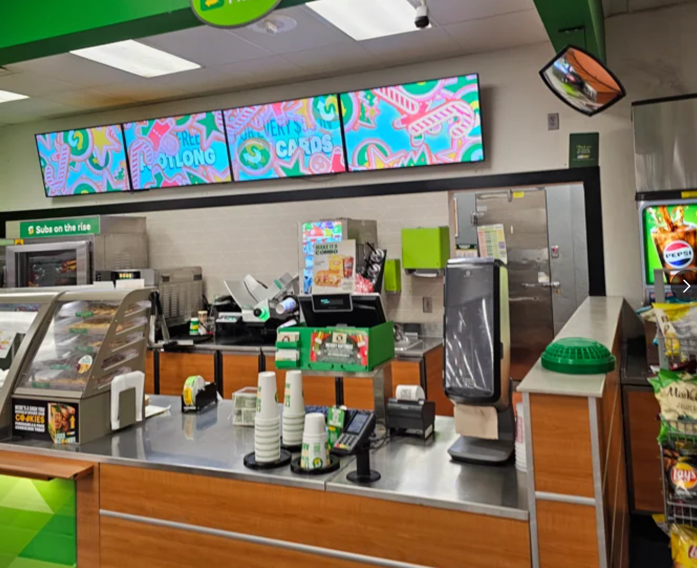 Interior of a sandwich shop with digital menu boards, a counter with a cash register, and cup dispensers in a clean, organized setting