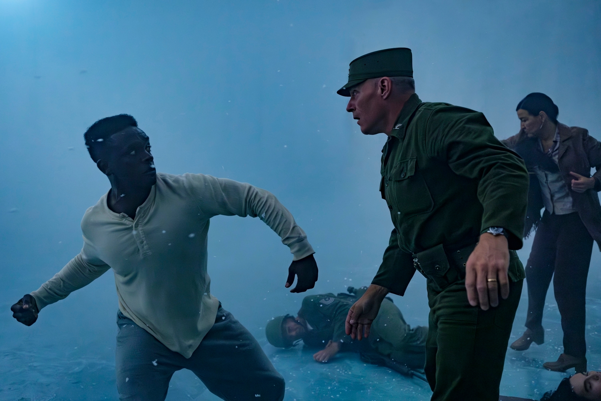 Men in a tense standoff with others in the background, one in military uniform. The setting appears chaotic and intense