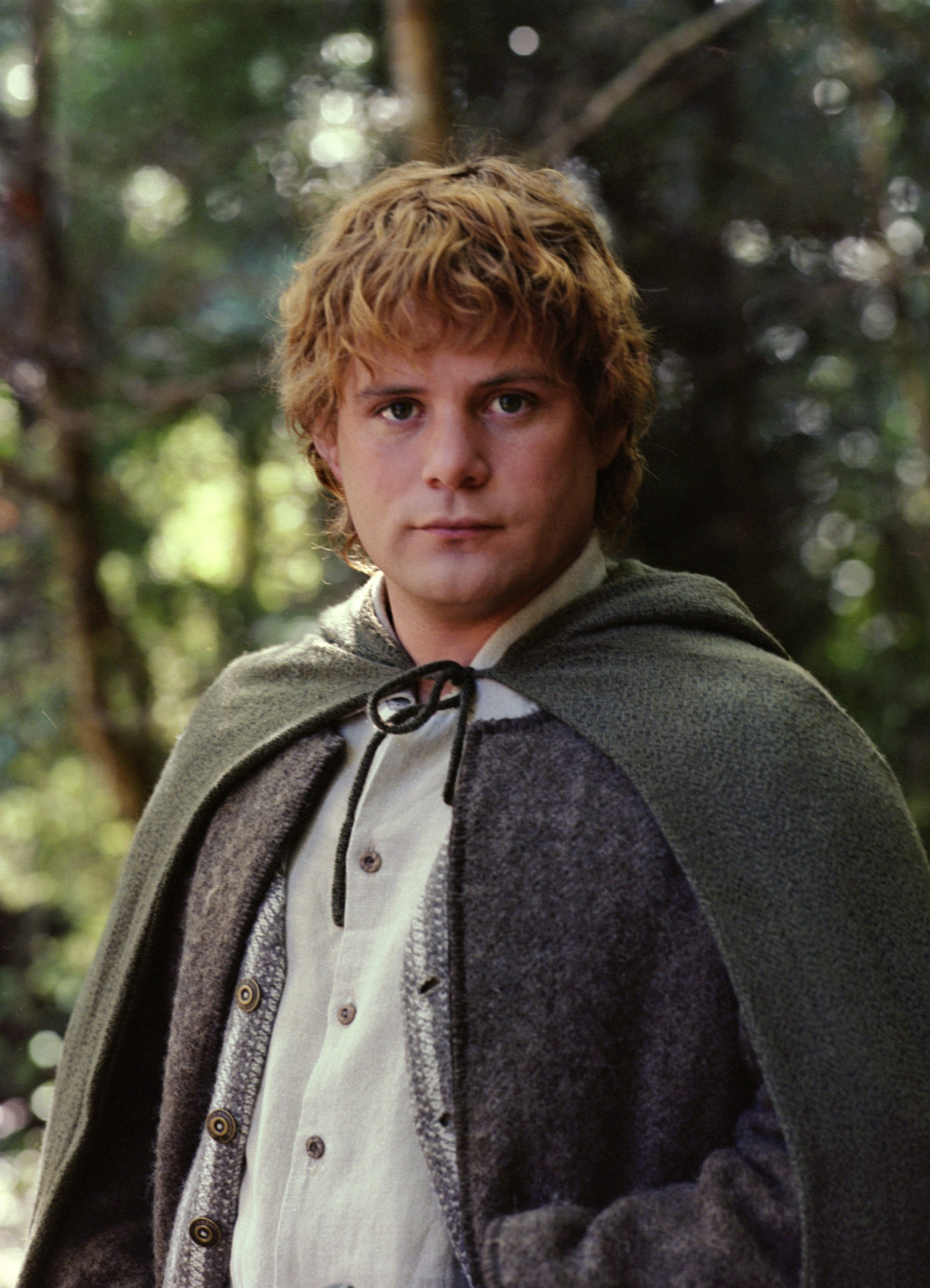 Person in a fantasy setting wearing a cloak and tunic, standing in a forest background