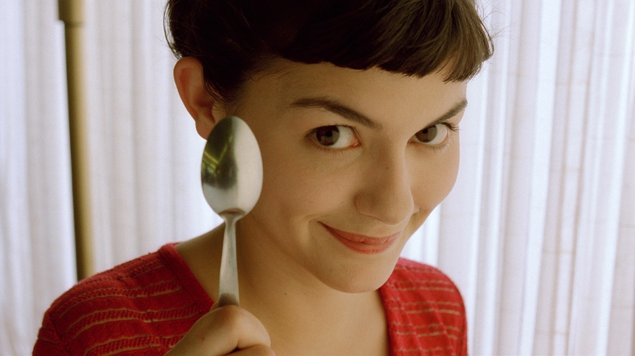 Person playfully holding a spoon near their face, smiling with short hair and a textured top