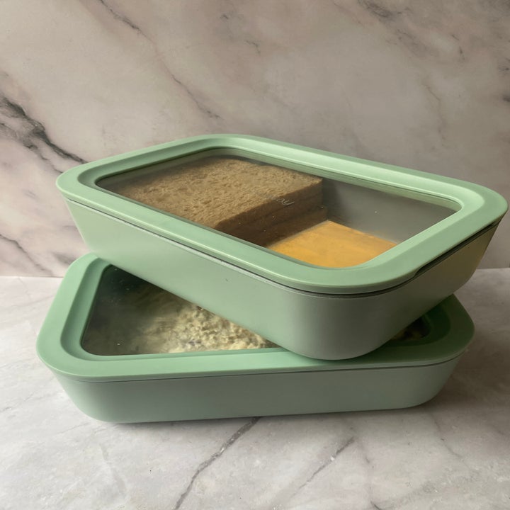 Two stacked green containers with clear lids showing a sandwich and other food inside