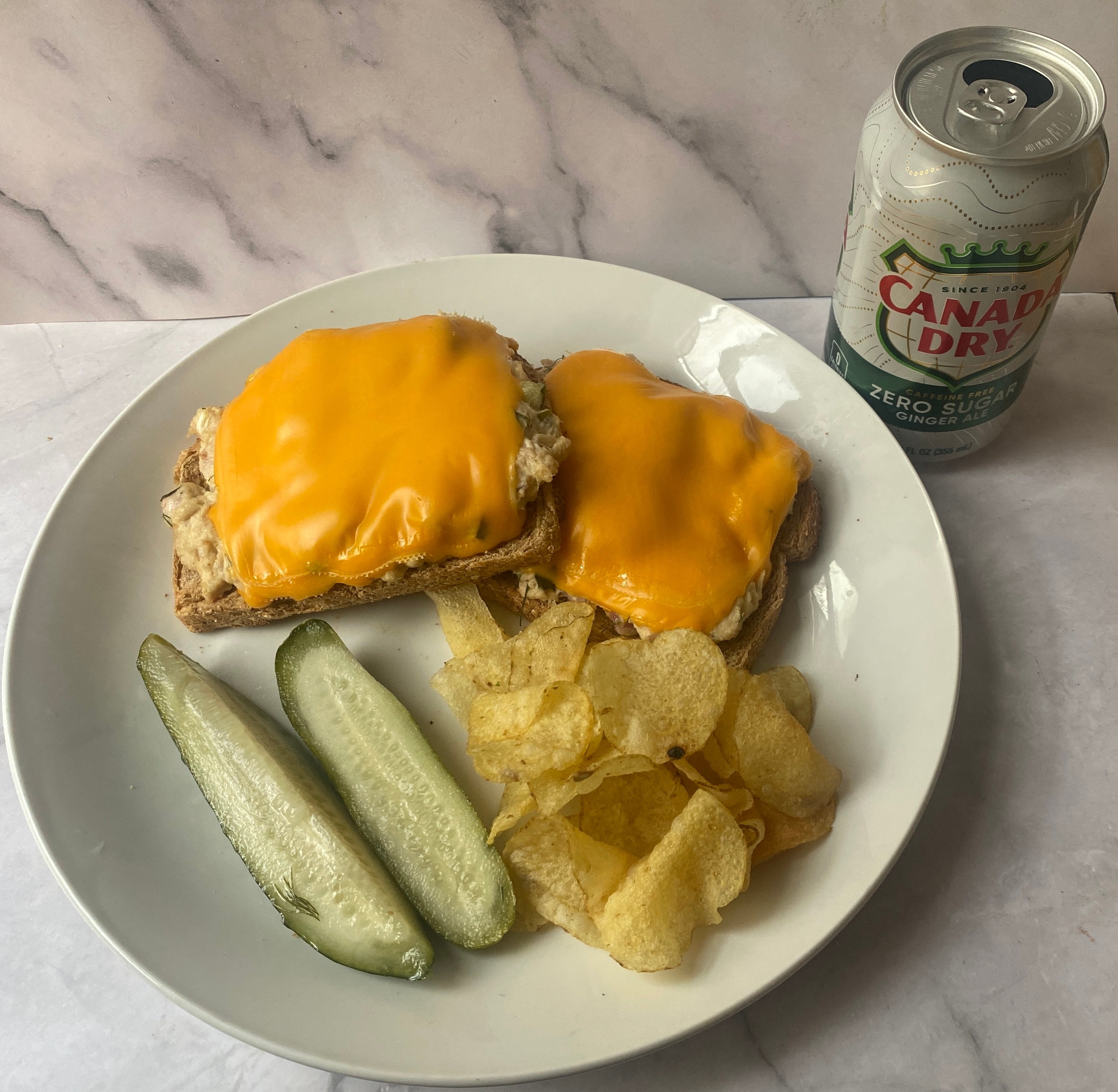 Plate with two open-faced grilled cheese sandwiches, potato chips, pickle spears, and a can of Canada Dry