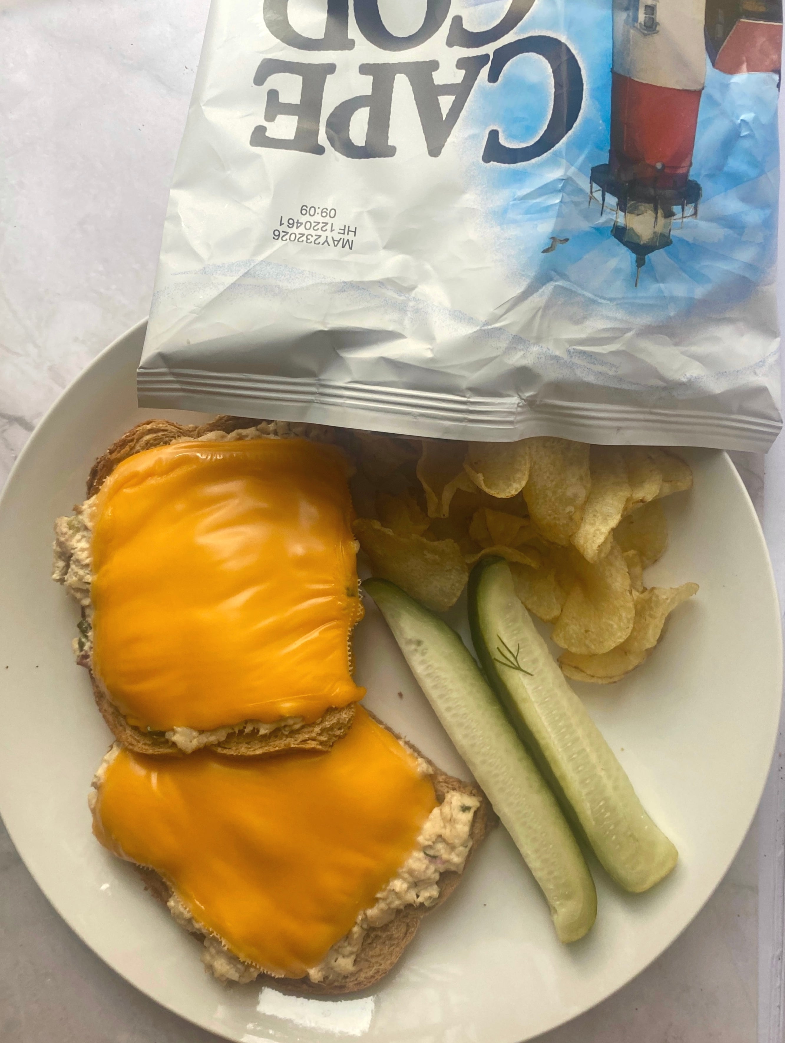 Plate with two tuna melts topped with cheese, pickle spears, and potato chips. A Cape Cod chip bag is nearby