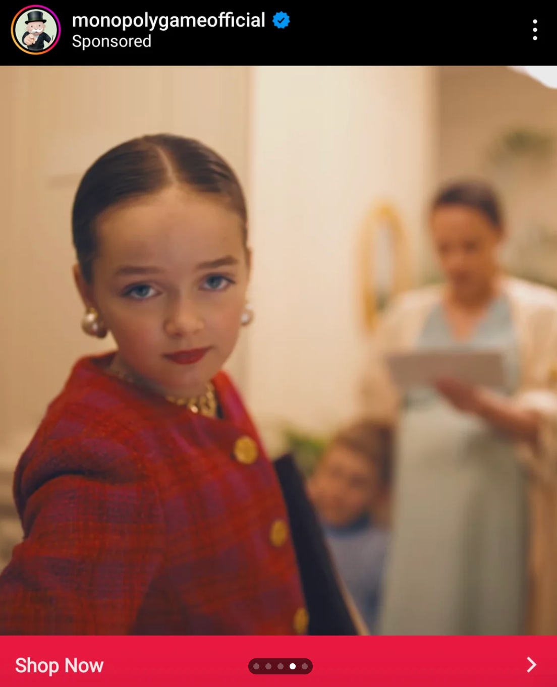 Child poses confidently in stylish attire with two adults in the background, one holding a tablet