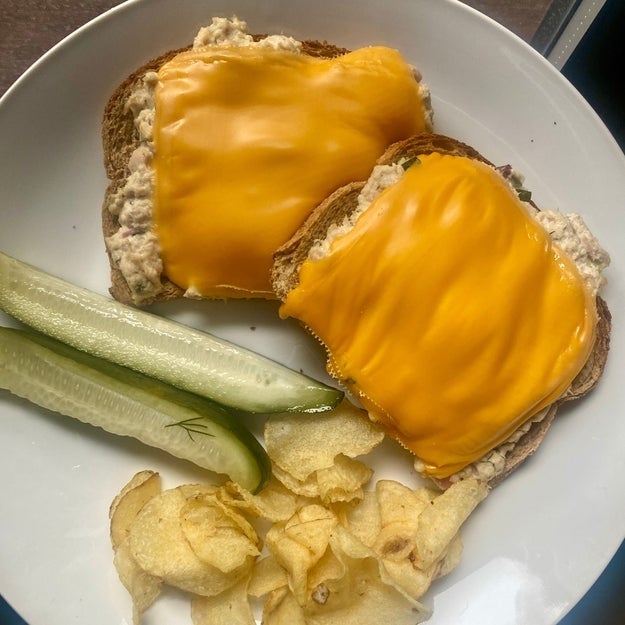 Two open-faced sandwiches with melted cheese on a plate, accompanied by pickle spears and potato chips