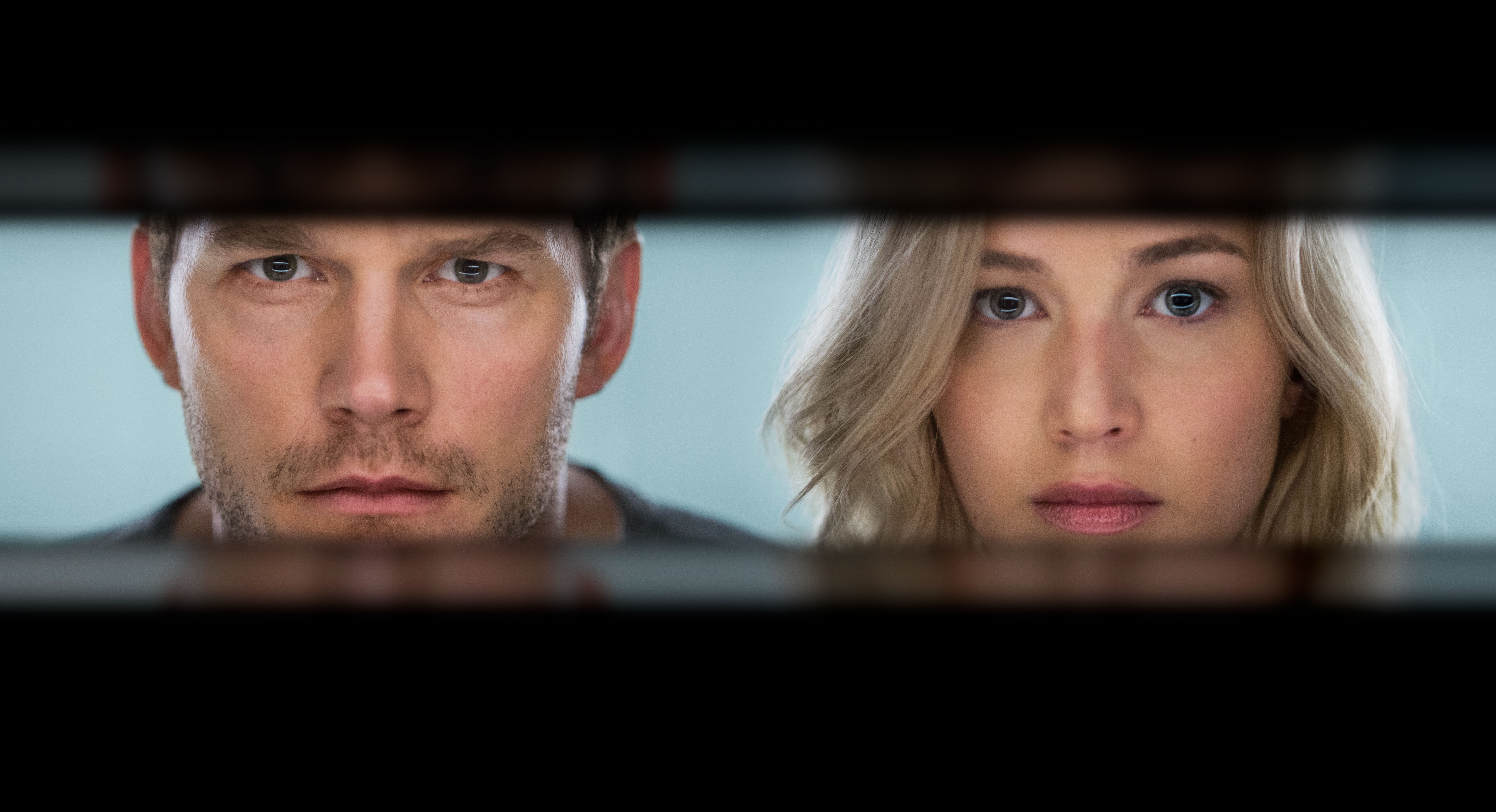 A man and a woman are seen through horizontal slats, both with serious expressions, suggesting they are looking through blinds or a similar structure