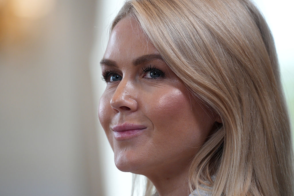 Person with long blonde hair smiling slightly, looking to the side. Light background