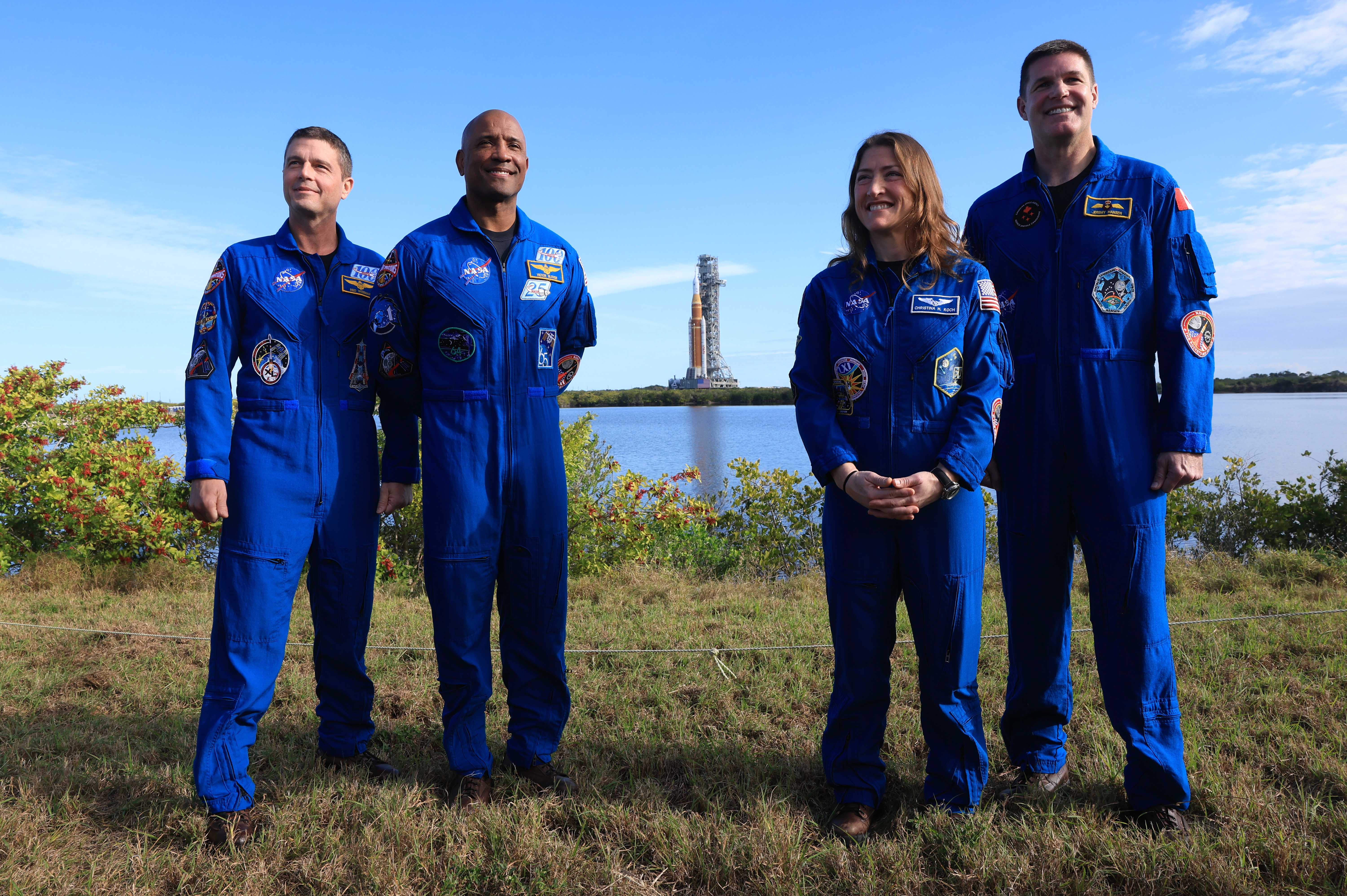 Four astronauts successful bluish formation suits basal outdoors, smiling, with a rocket successful the background
