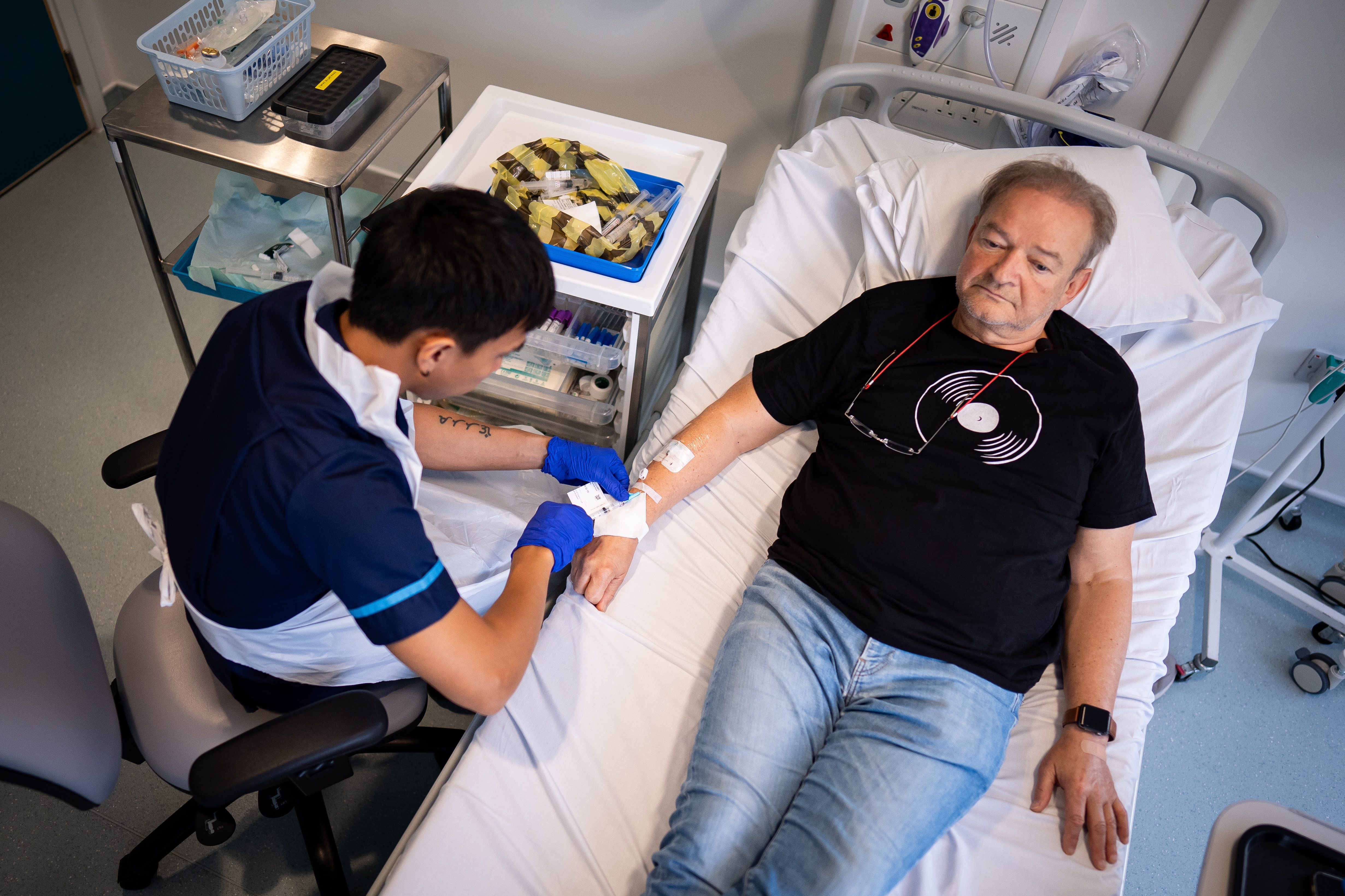 Person receiving an IV successful a objective setting, wearing a t-shirt with a grounds design, attended by a healthcare worker
