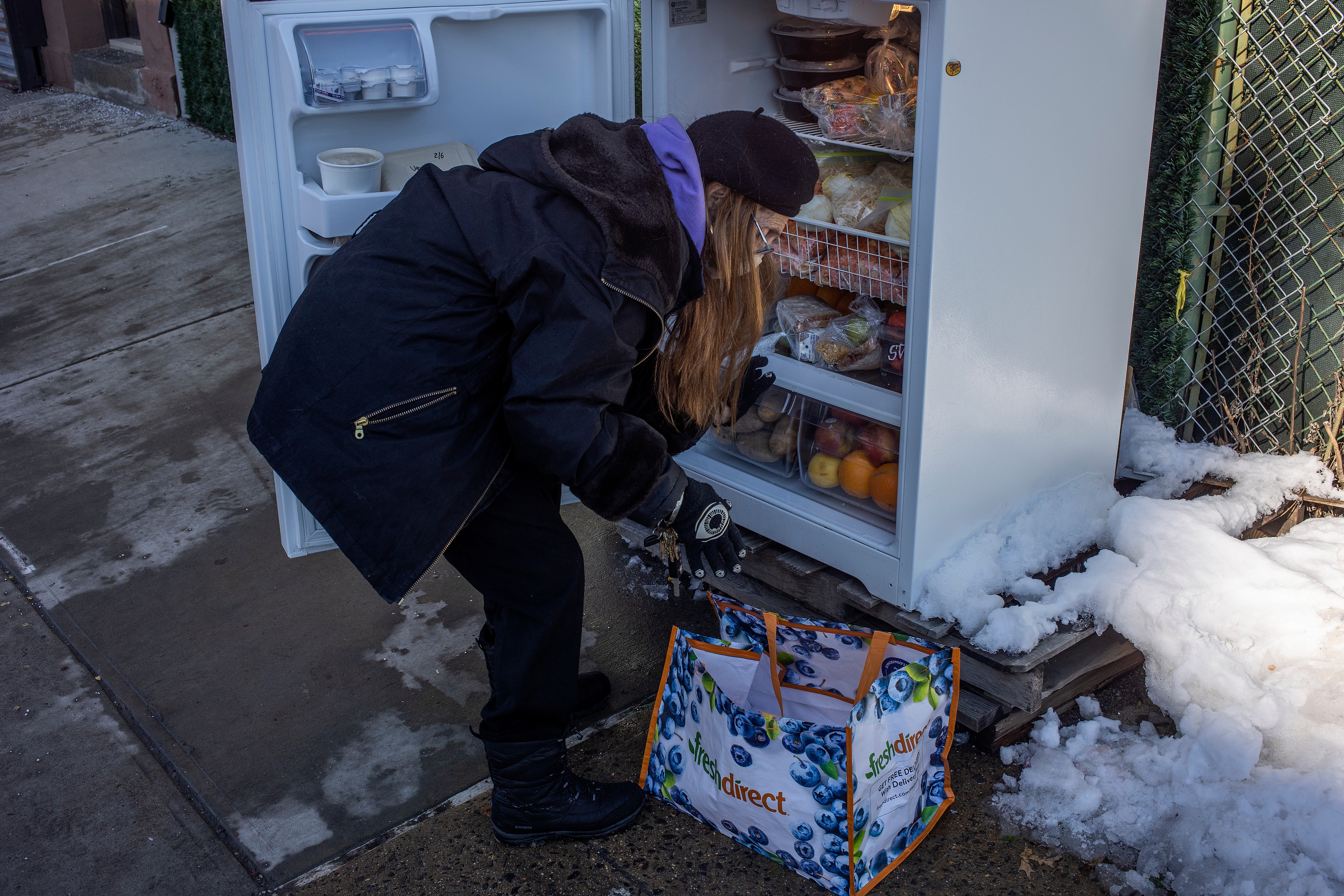 Person successful wintertime covering places nutrient successful an outdoor assemblage fridge, with snowfall connected the crushed and a reusable container nearby