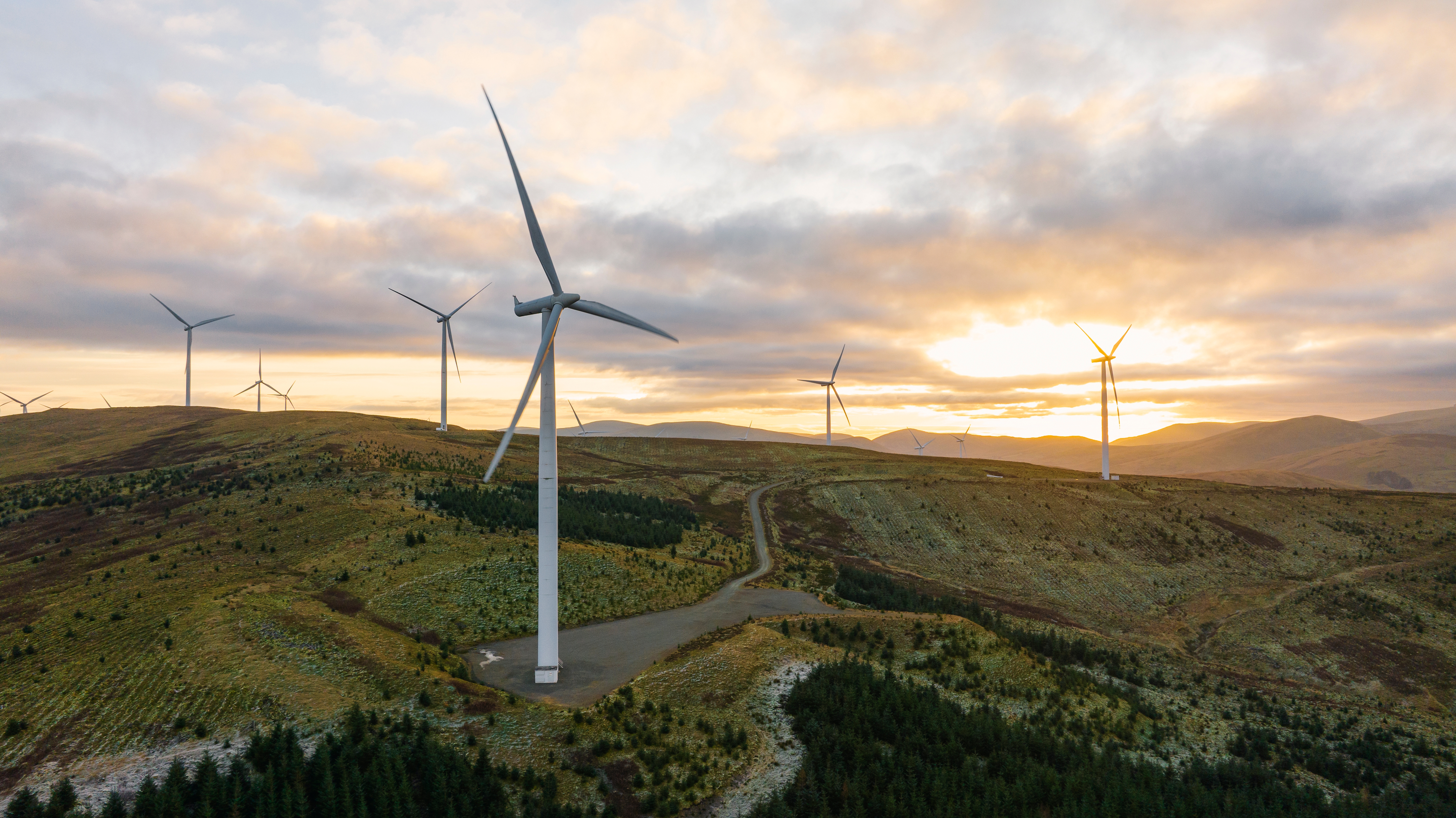 Wind turbines connected a grassy elevation during sunrise, with respective turbines successful the region nether a partially cloudy sky