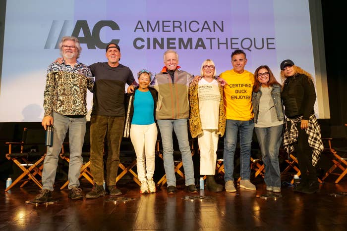 Group of eight people standing together, casually dressed, in front of an "American Cinematheque" backdrop at a panel or event
