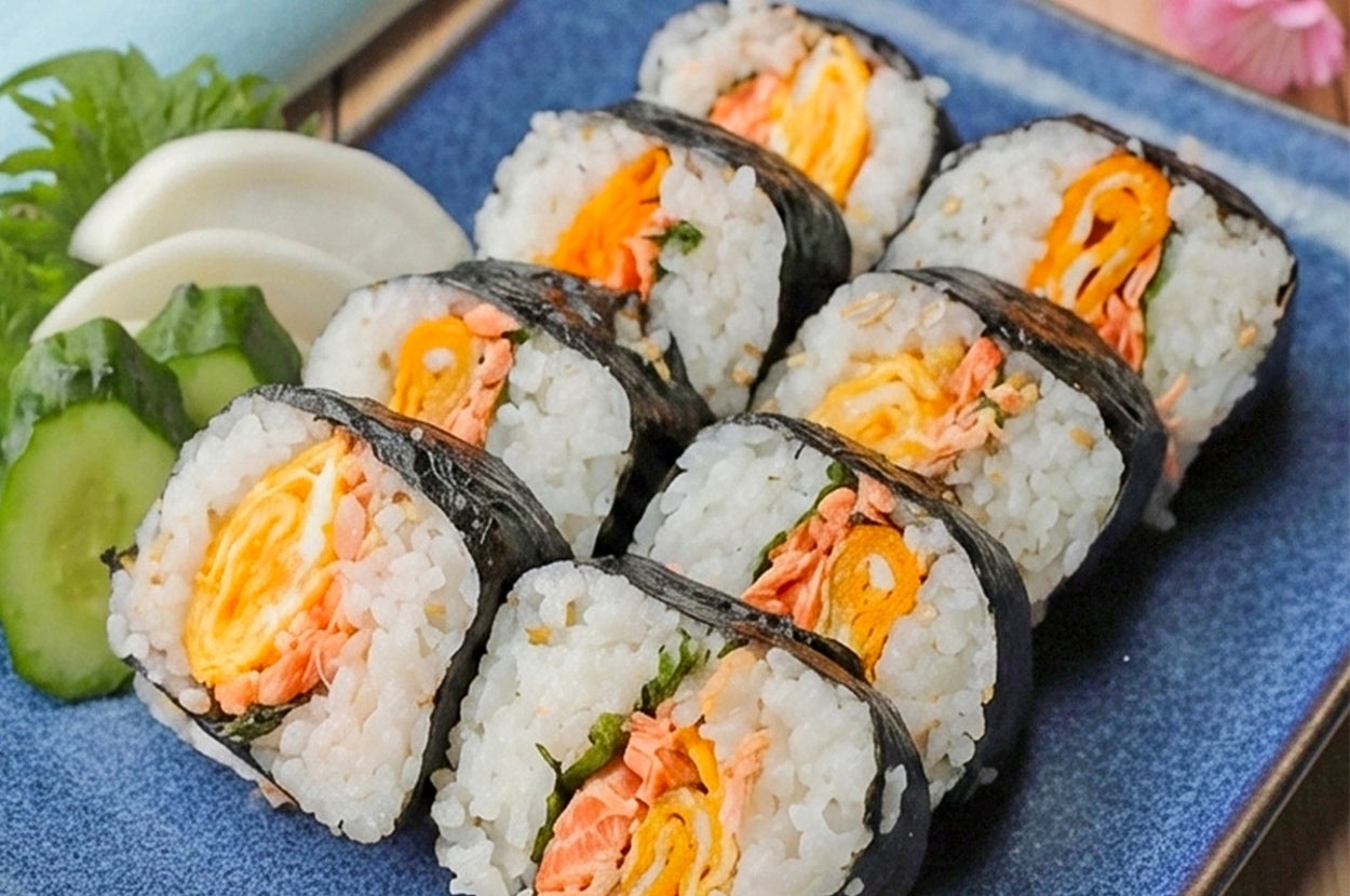 お皿に盛られた8個の細巻き寿司。具に玉子焼きと魚。添えられた野菜の飾りつけ。テーブルに置かれている。