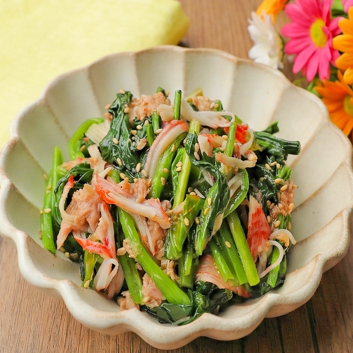 器に盛られた和風サラダ。ほうれん草、カニカマ、ゴマが混ざっている。背景に花が添えられている。