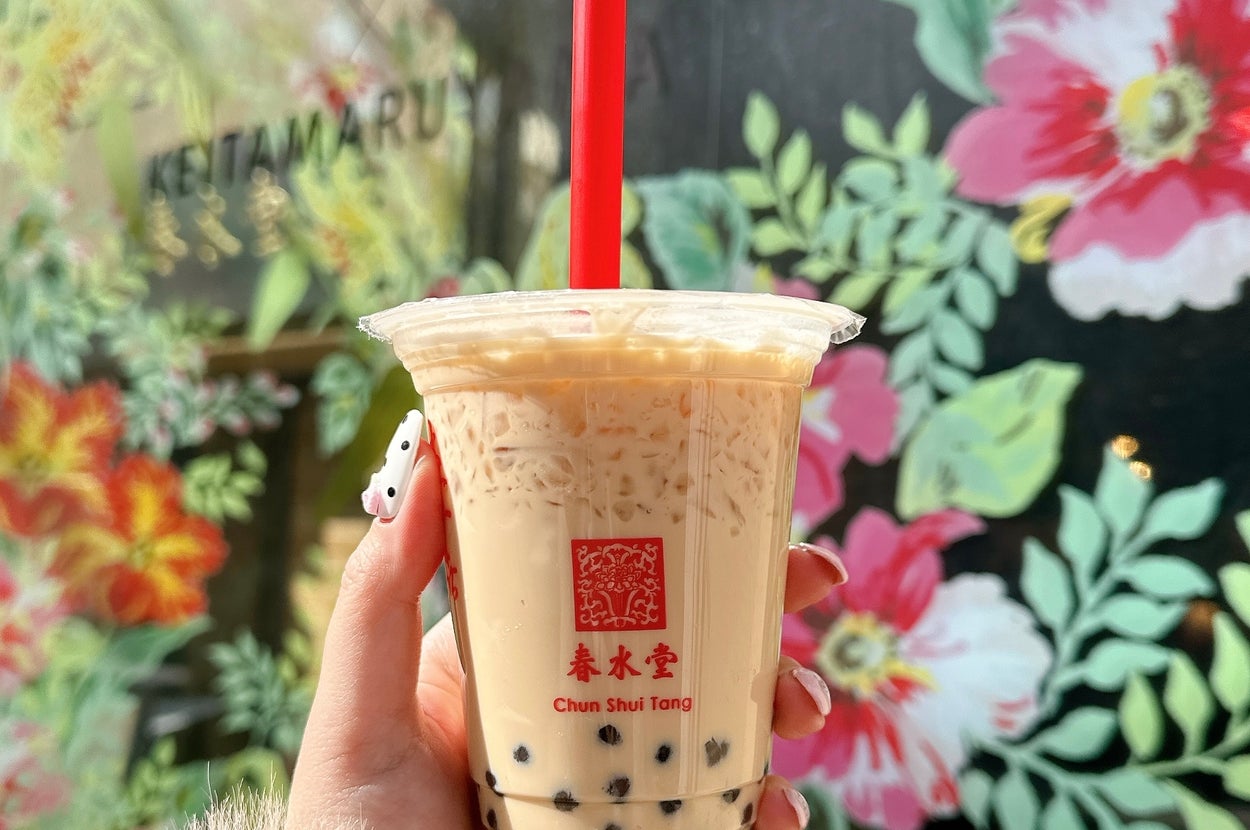 タピオカミルクティーを持つ手。背景に花の壁画がある。