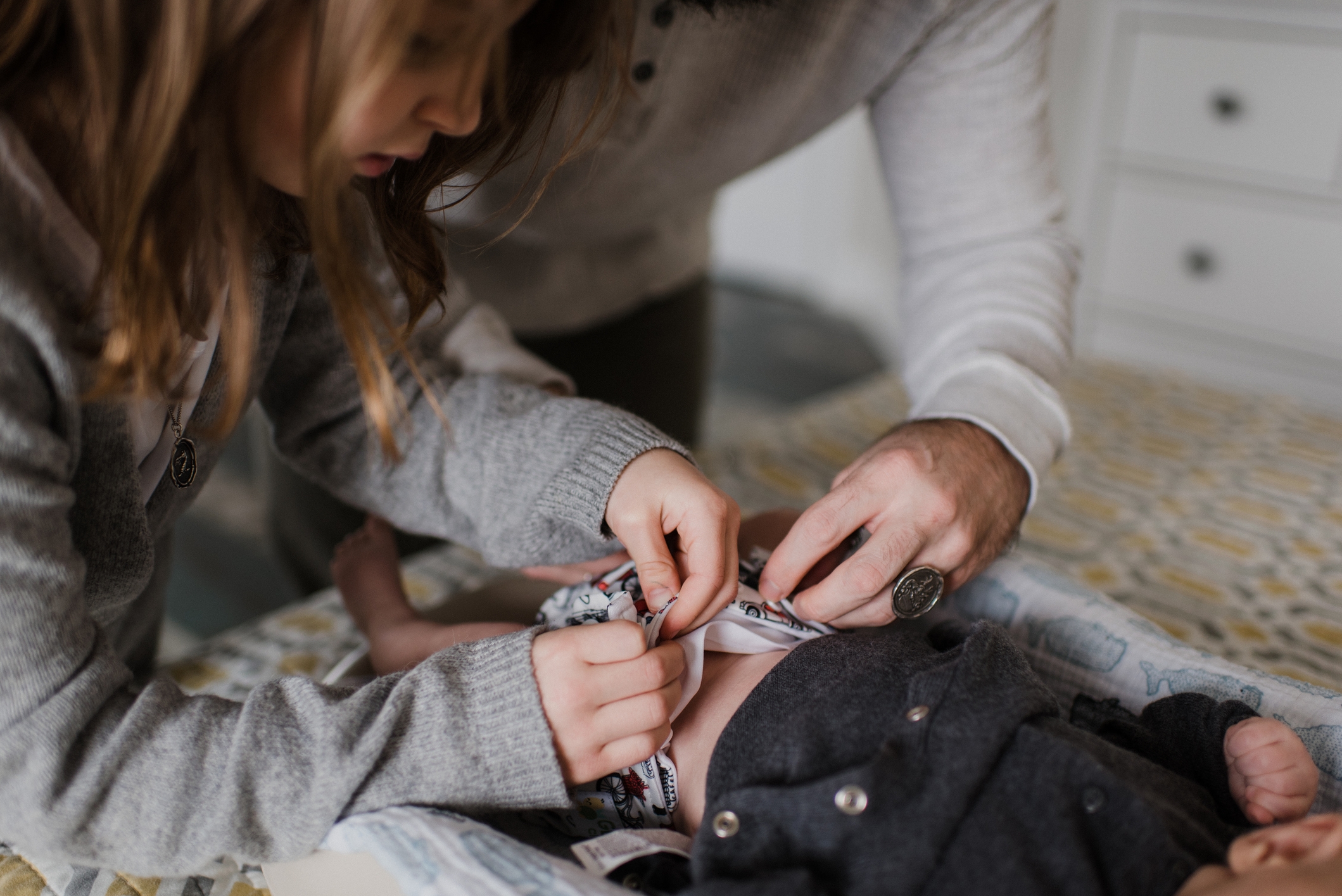 Child and adult gently change a baby's diaper on a changing table, showcasing a caring and nurturing moment