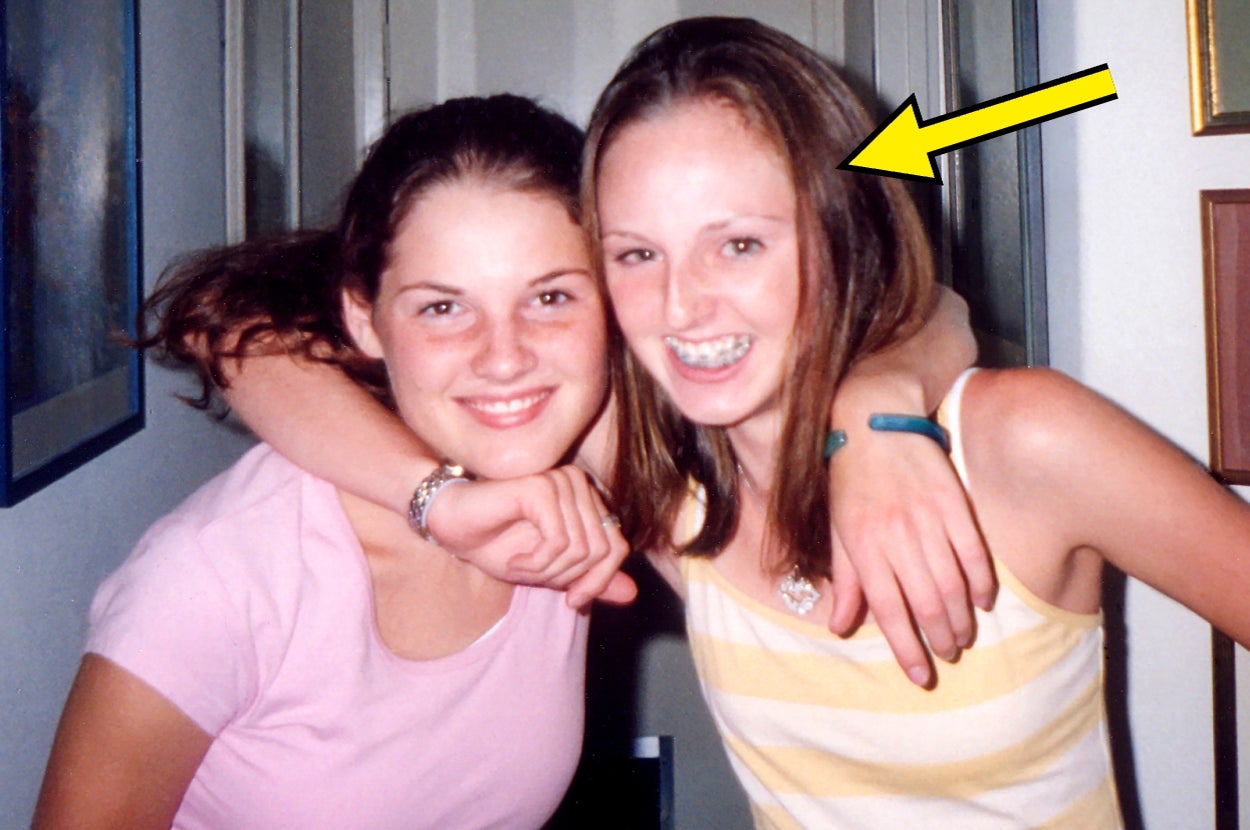 Two smiling young women pose together indoors. The woman on the right has an arrow pointing at her, both dressed casually