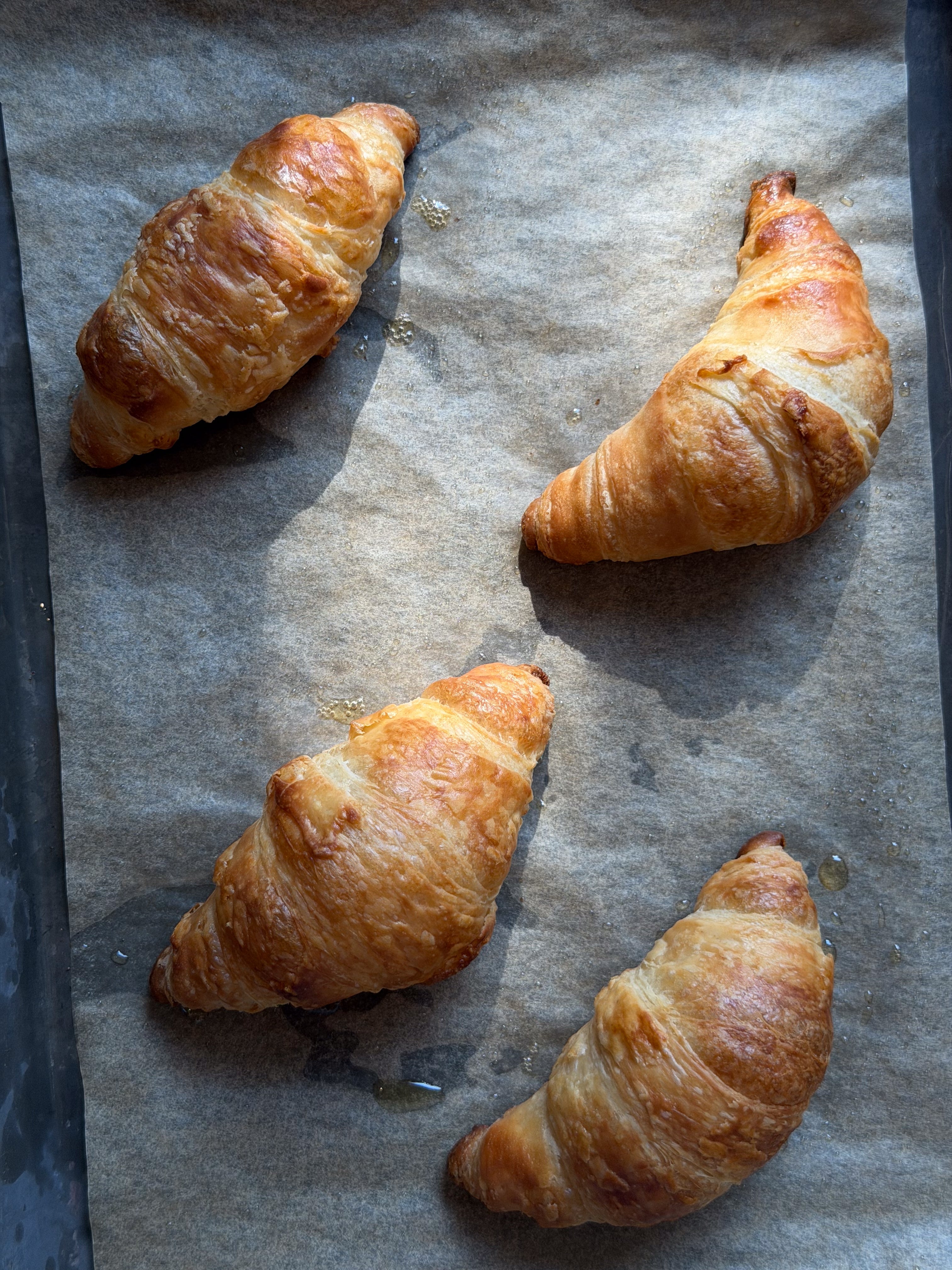 Four freshly baked croissants on a parchment-lined baking tray