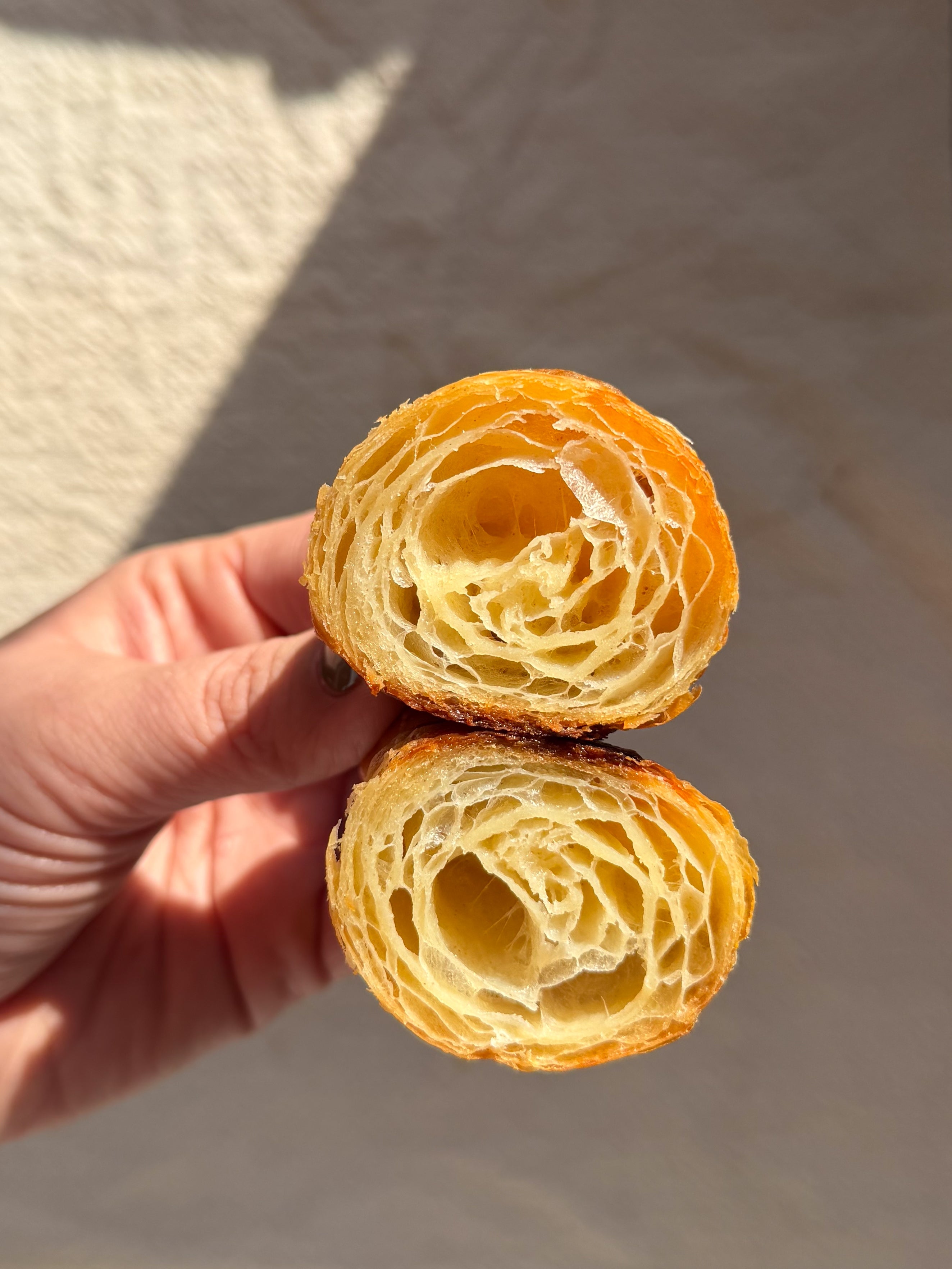 Hand holding a sliced croissant with a flaky, layered interior, shown against a neutral background